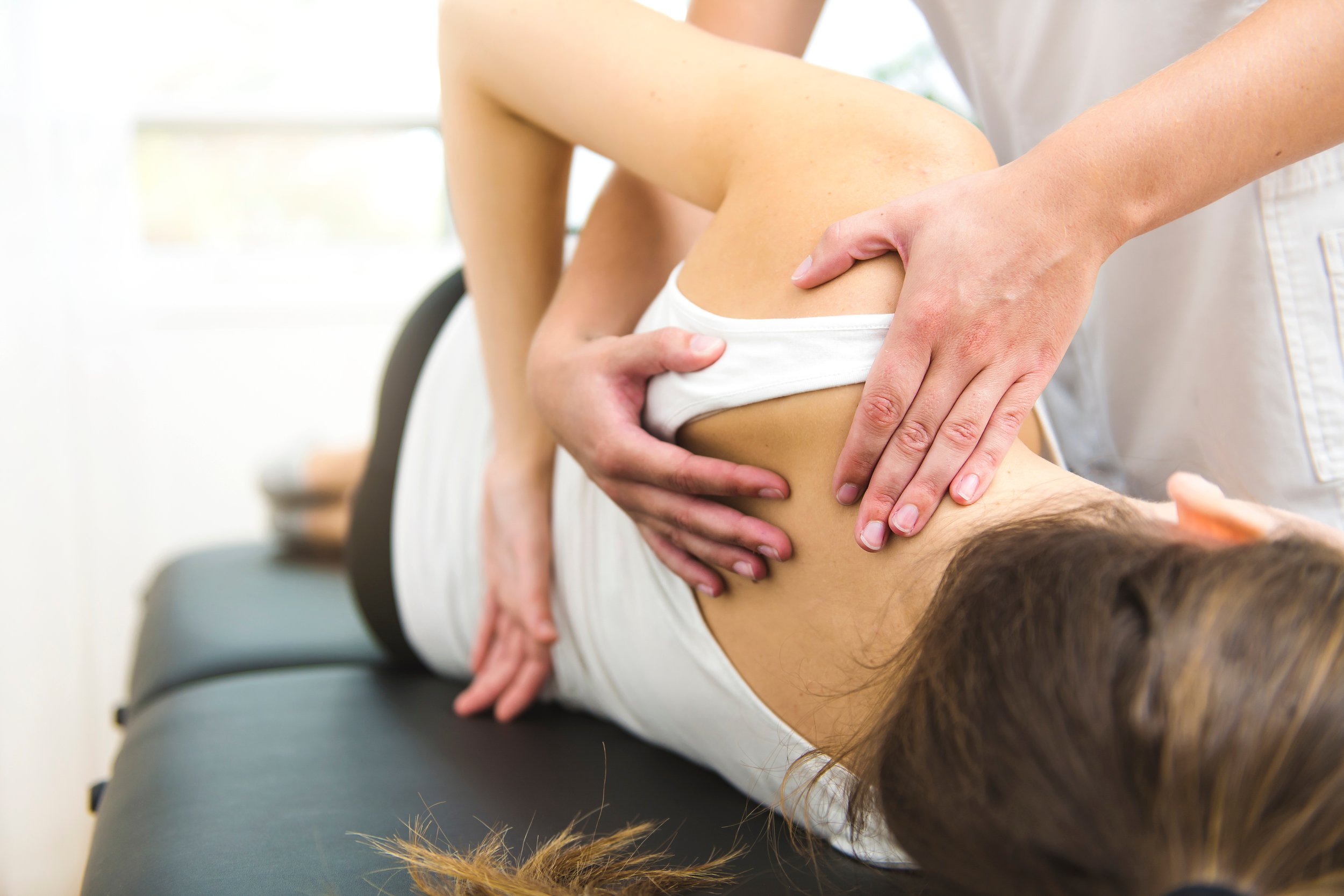 Healthcare professional performing physical therapy or examination on a patient's shoulder while lying down.