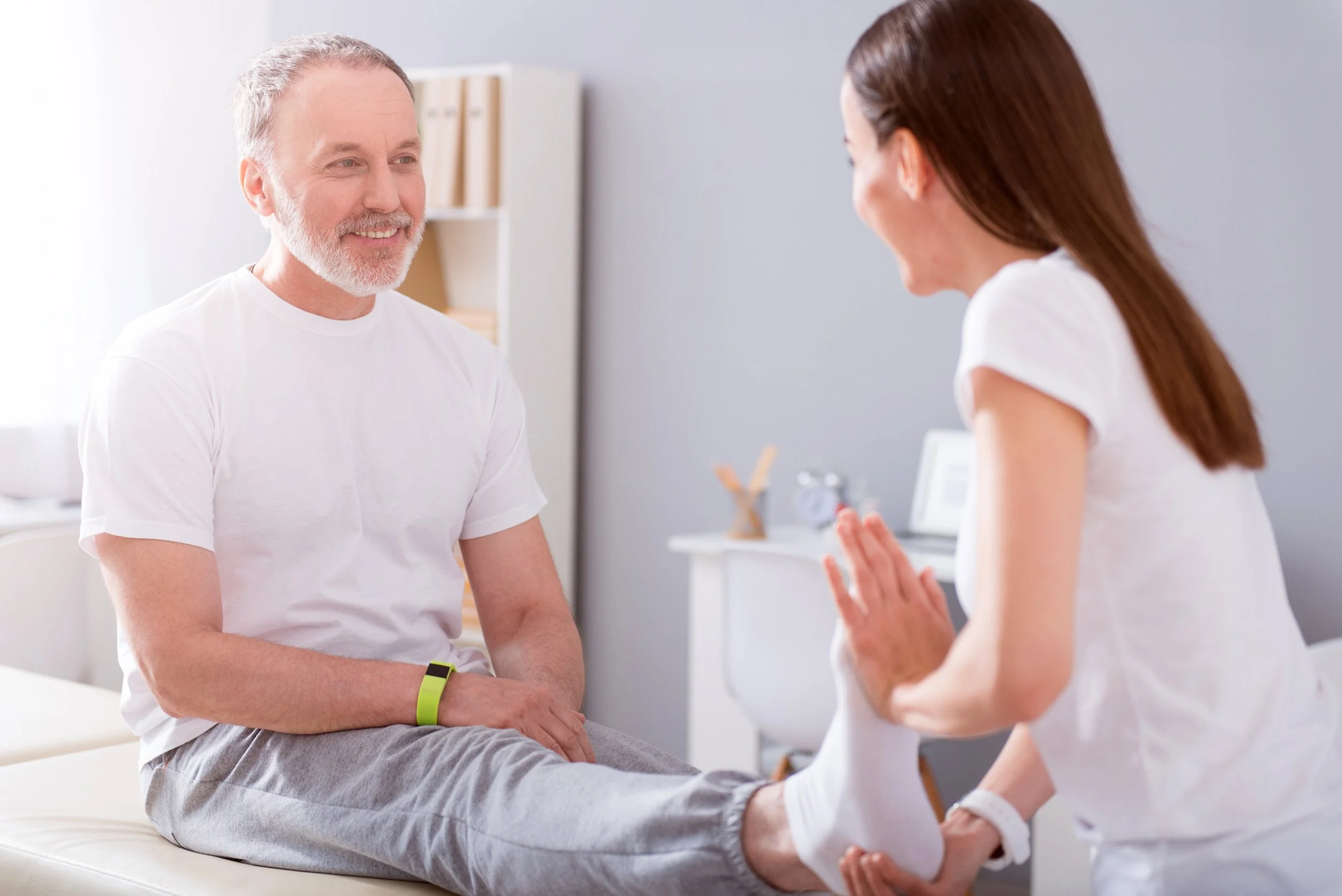 A healthcare professional performs a physical therapy exercise with a senior male patient in a bright, modern clinic setting.
