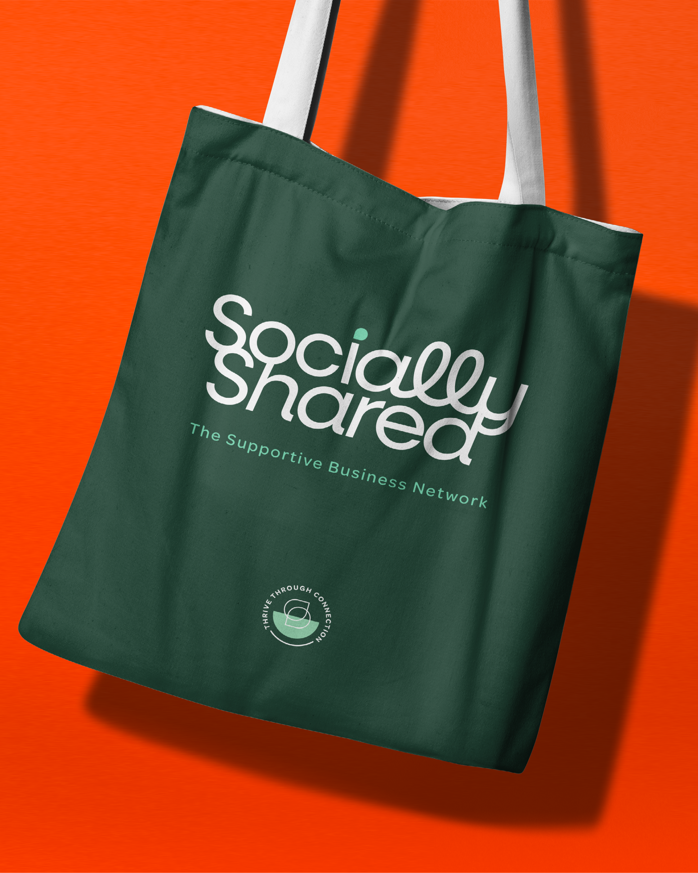 Green tote bag with white and turquoise text reading "Socially Shared, The Supportive Business Network" on an orange background.