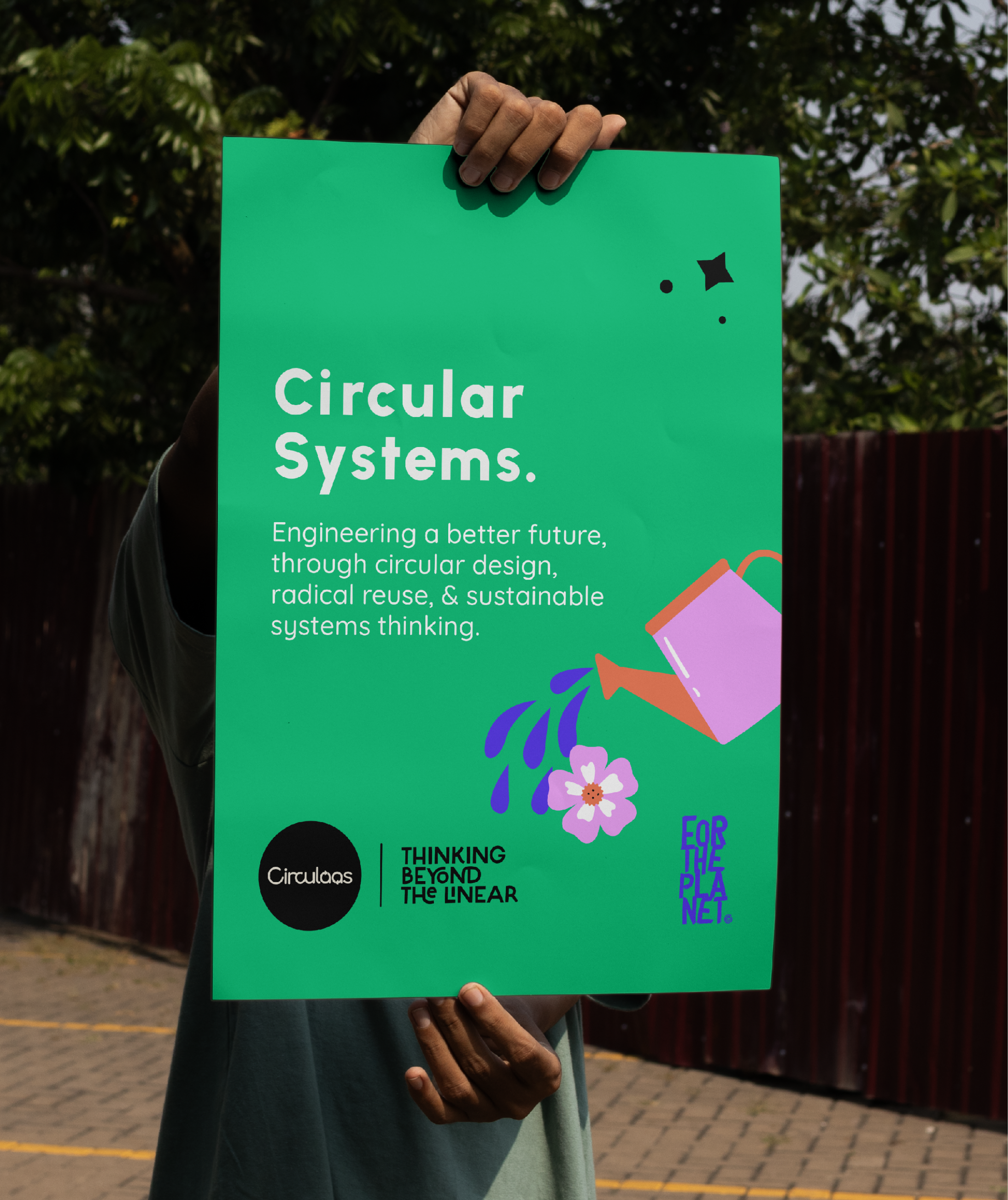 Person holding a green poster with white and black text and illustrations about circular systems outdoors.