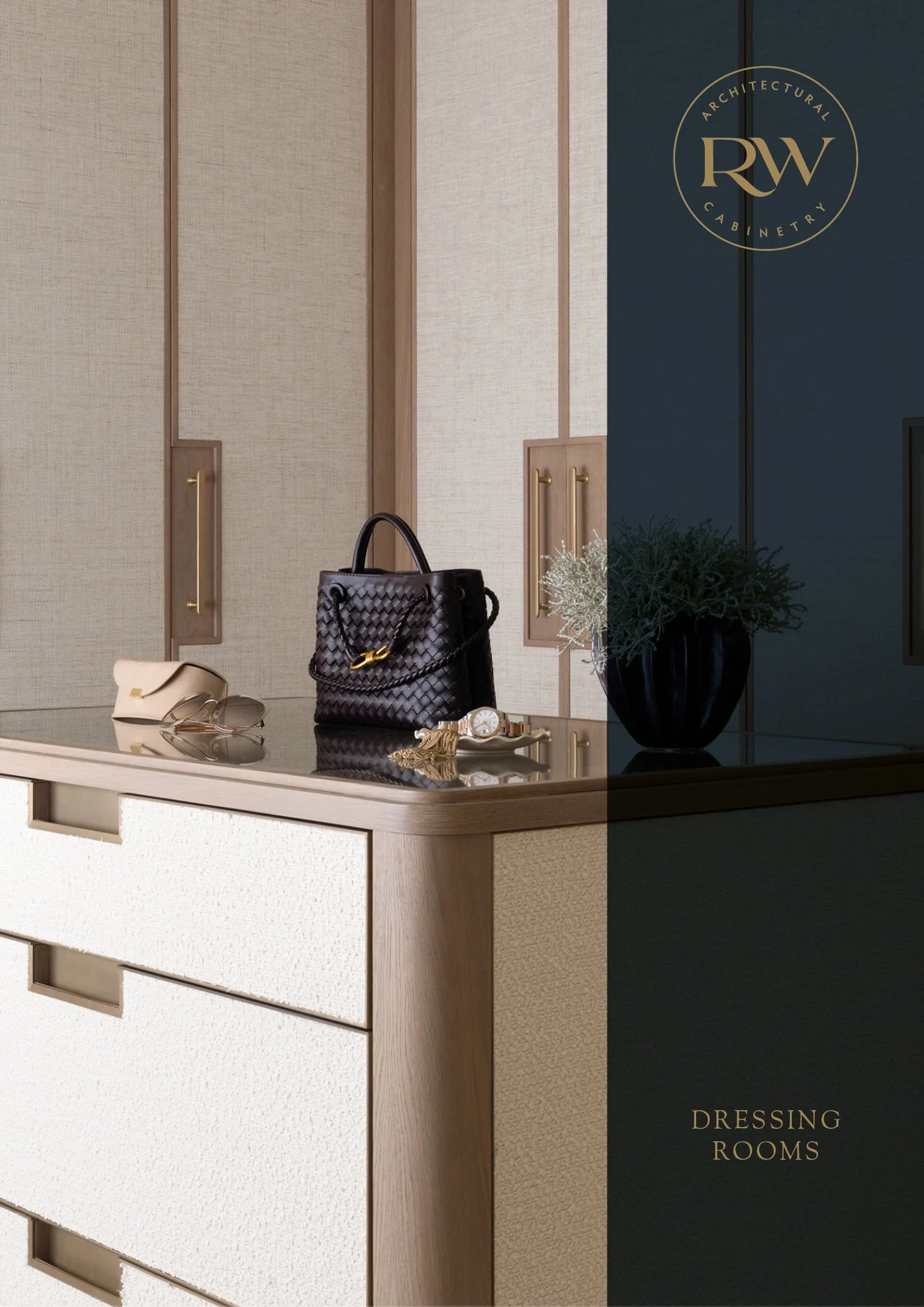 A dressing room reception desk with a beige and wood finish, displaying a black woven handbag, beige wallet, sunglasses, a gold watch, and jewelry; a dark blue flowerpot with greenery; a logo reading "RW Architectural Cabinetry" in gold at the top right corner; the words "Dressing Rooms" in gold at the bottom right corner.