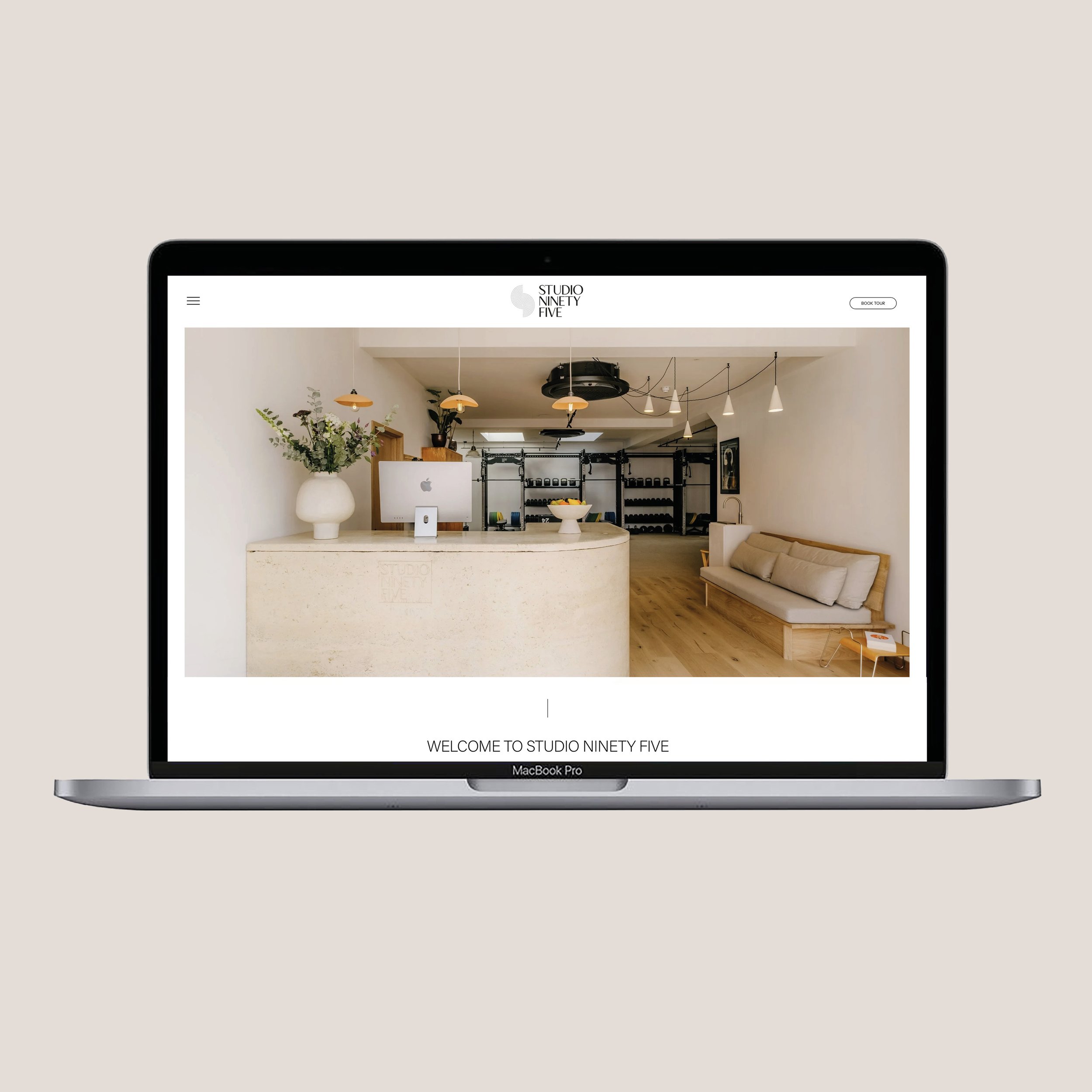 Laptop displaying the website of Studio Ninety Five with a minimalist reception area featuring a beige counter, a large white vase with flowers, a computer, and a cozy seating area with a beige sofa.