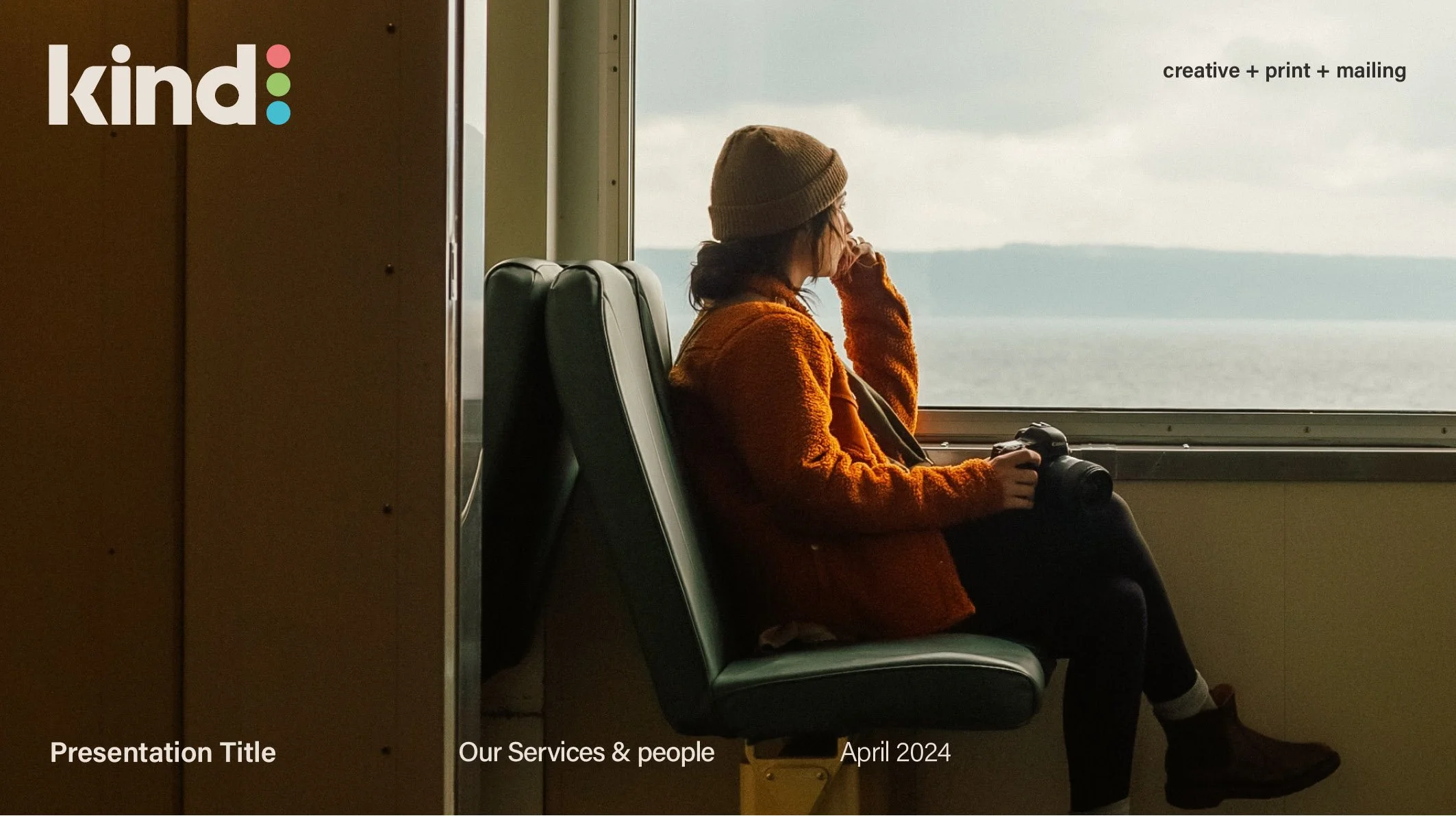 A woman sitting on a green airport bench, wearing a brown beanie and orange jacket, holding a camera, looking out the window at a body of water and distant land.