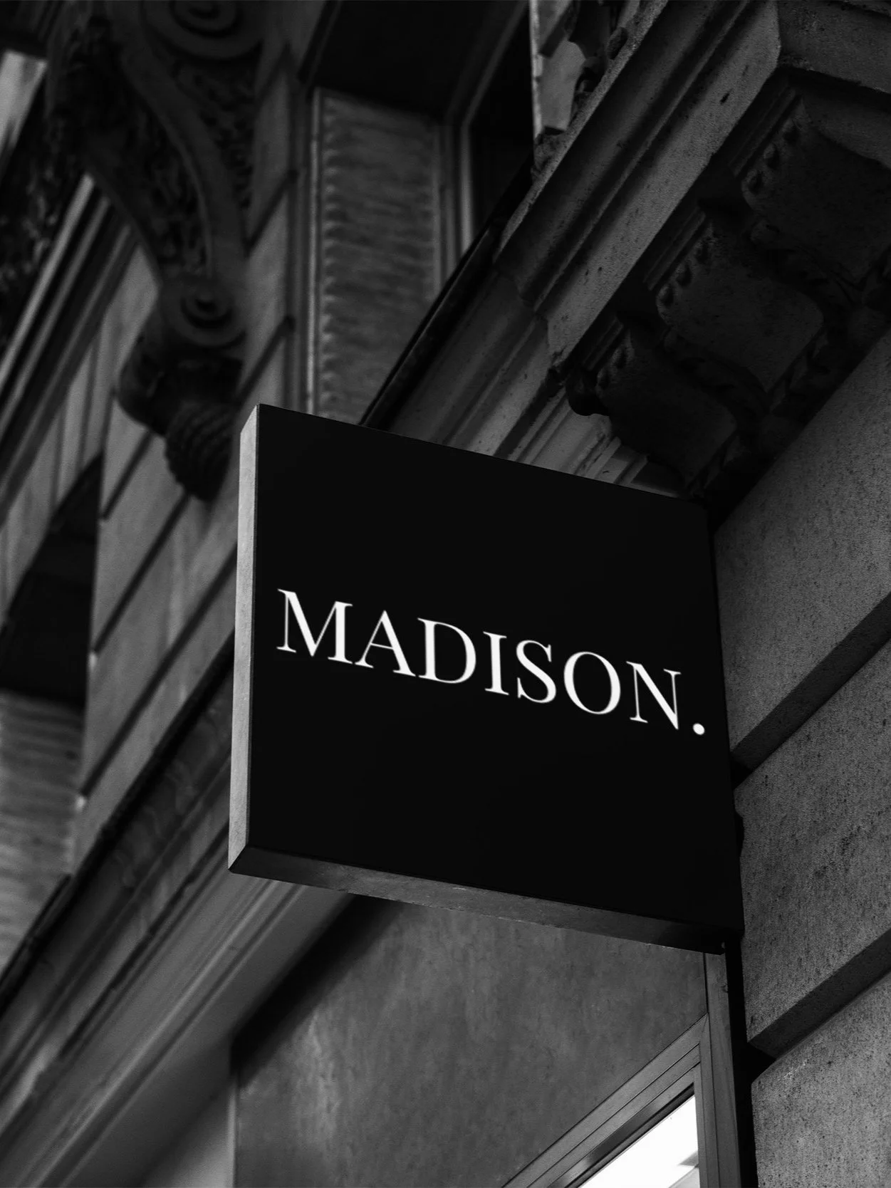 Black sign with white text reading "MADISON" hanging on a building facade.