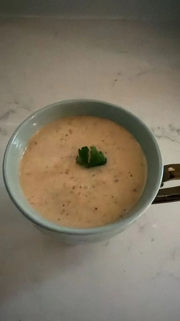 A light blue bowl containing a creamy soup garnished with a small sprig of cilantro, placed on a marble countertop.
