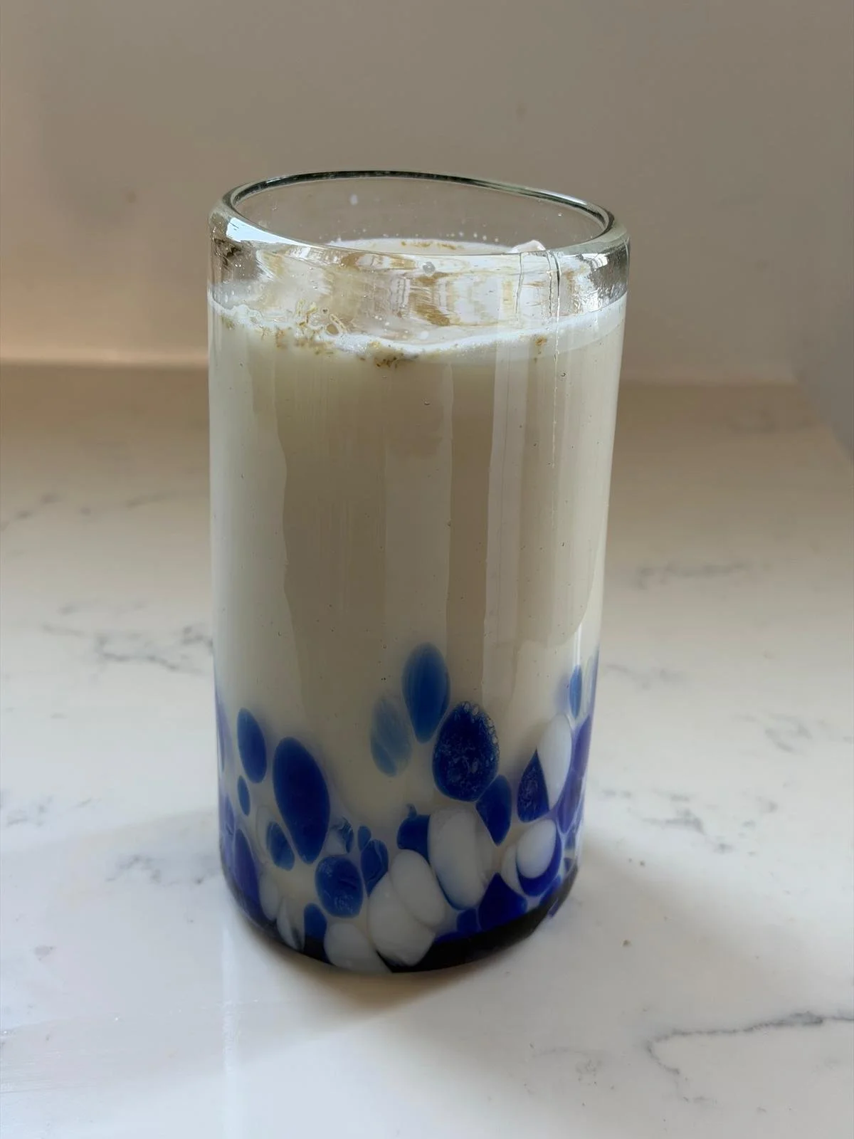 A tall glass of bubble tea with white and blue tapioca pearls at the bottom.