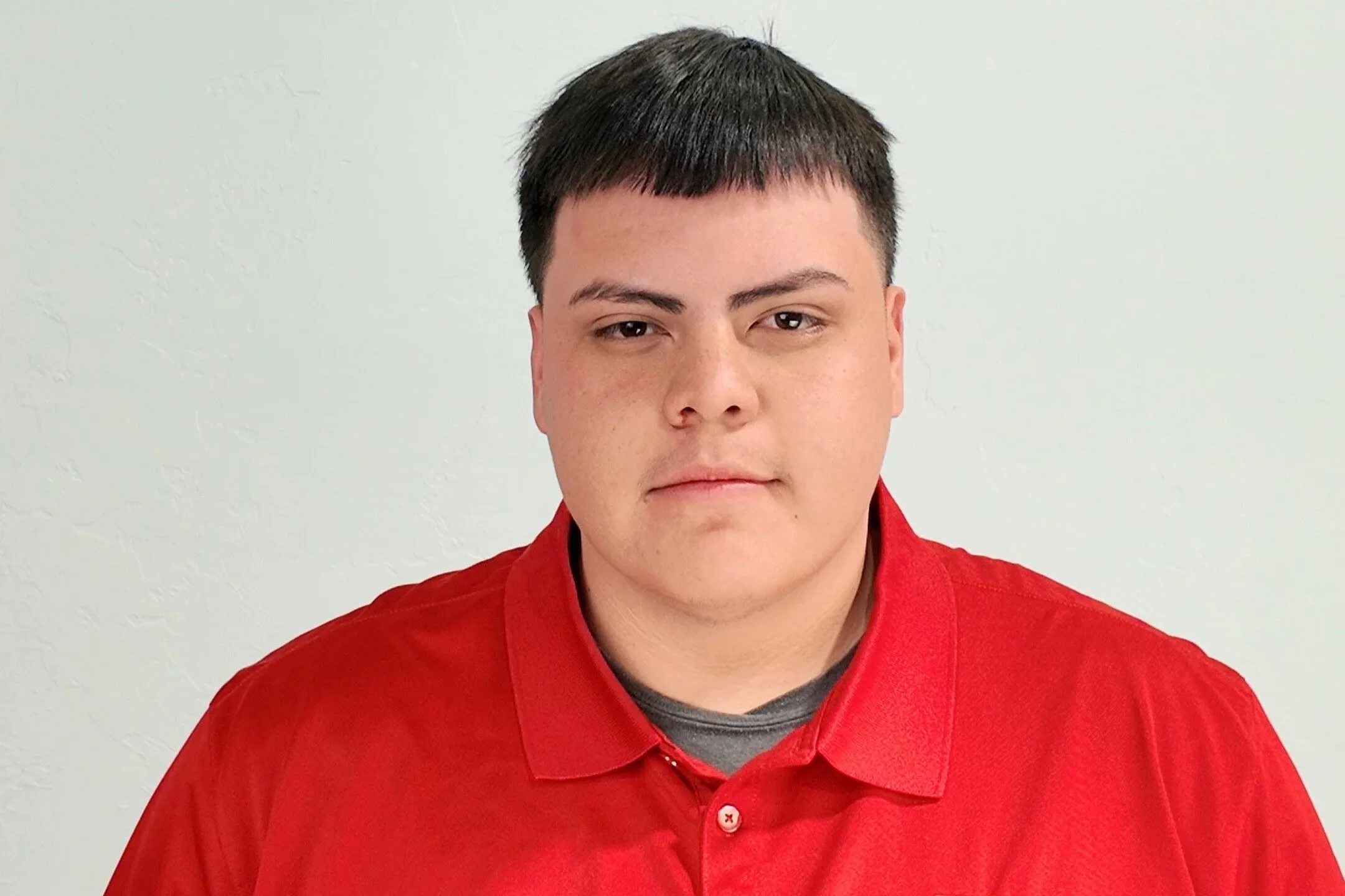 Young man wearing a gray trucker hat and a blue T-shirt with an A&T Mechanical logo, posing against a gray textured background.