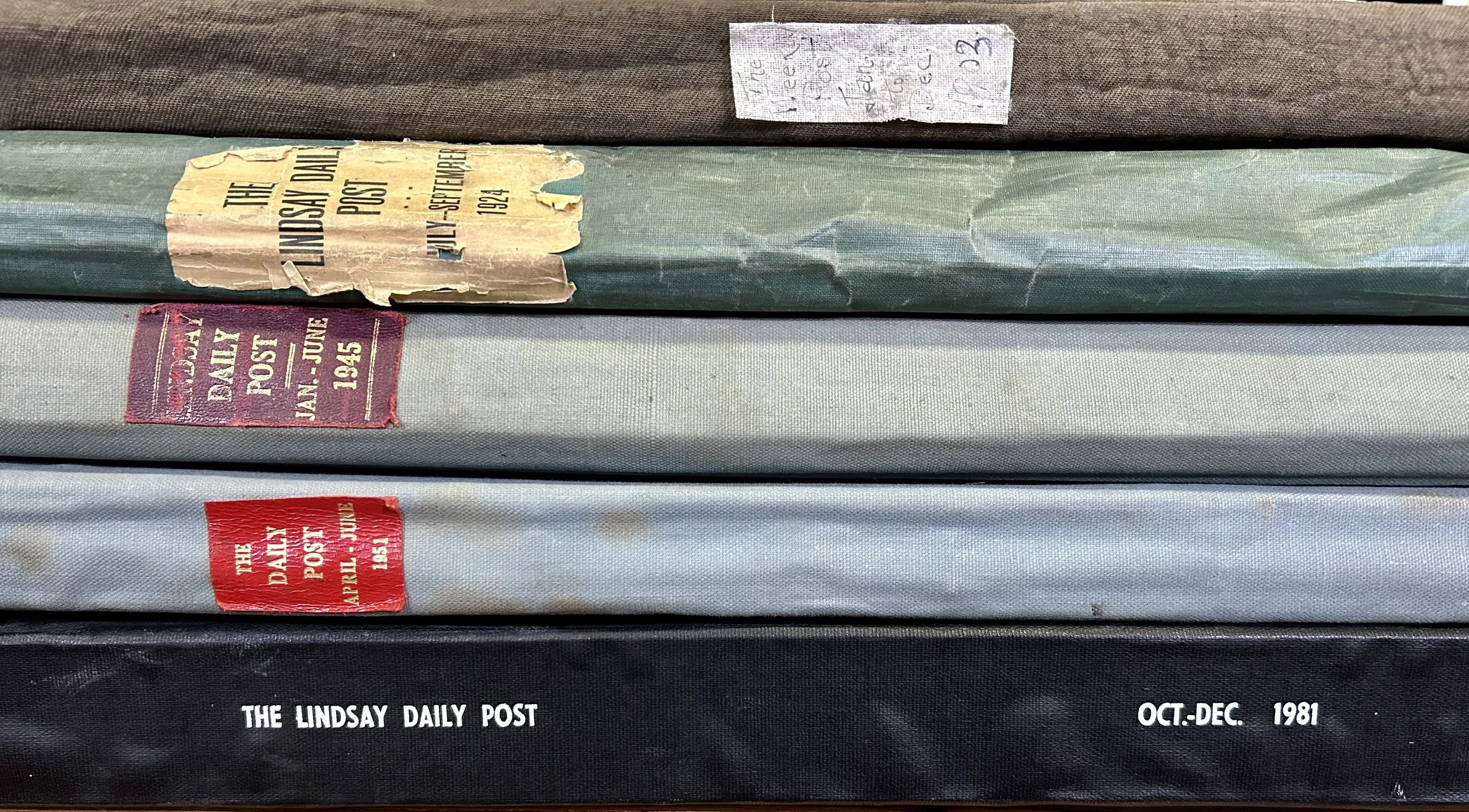 Stack of bound volumes of "The Lindsay Daily Post" with labels indicating various date ranges, including 1924, 1945, 1951, and 1981.