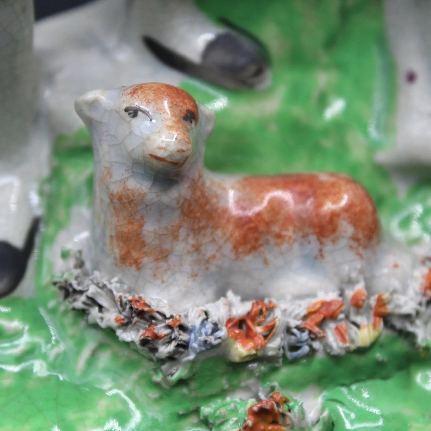 Ceramic figurine of a lamb lying on a green base with floral details.