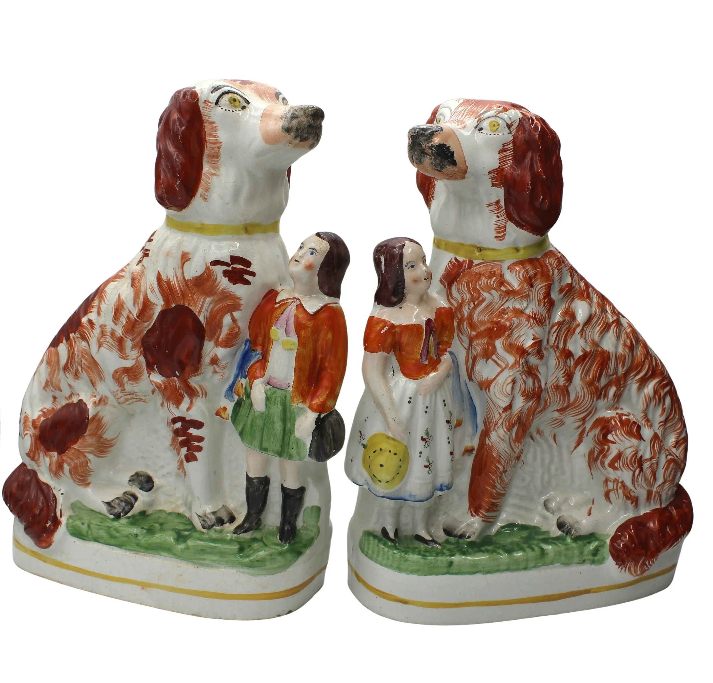 Two ceramic figurines of large dogs with brown patches next to smaller figurines of a man and a woman,