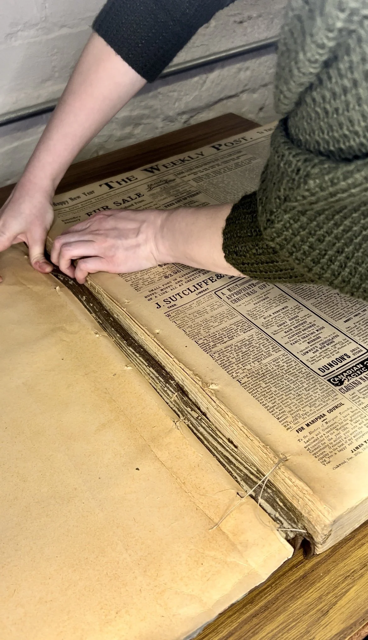 Person handling a vintage newspaper from "The Weekly Post" on a wooden table.