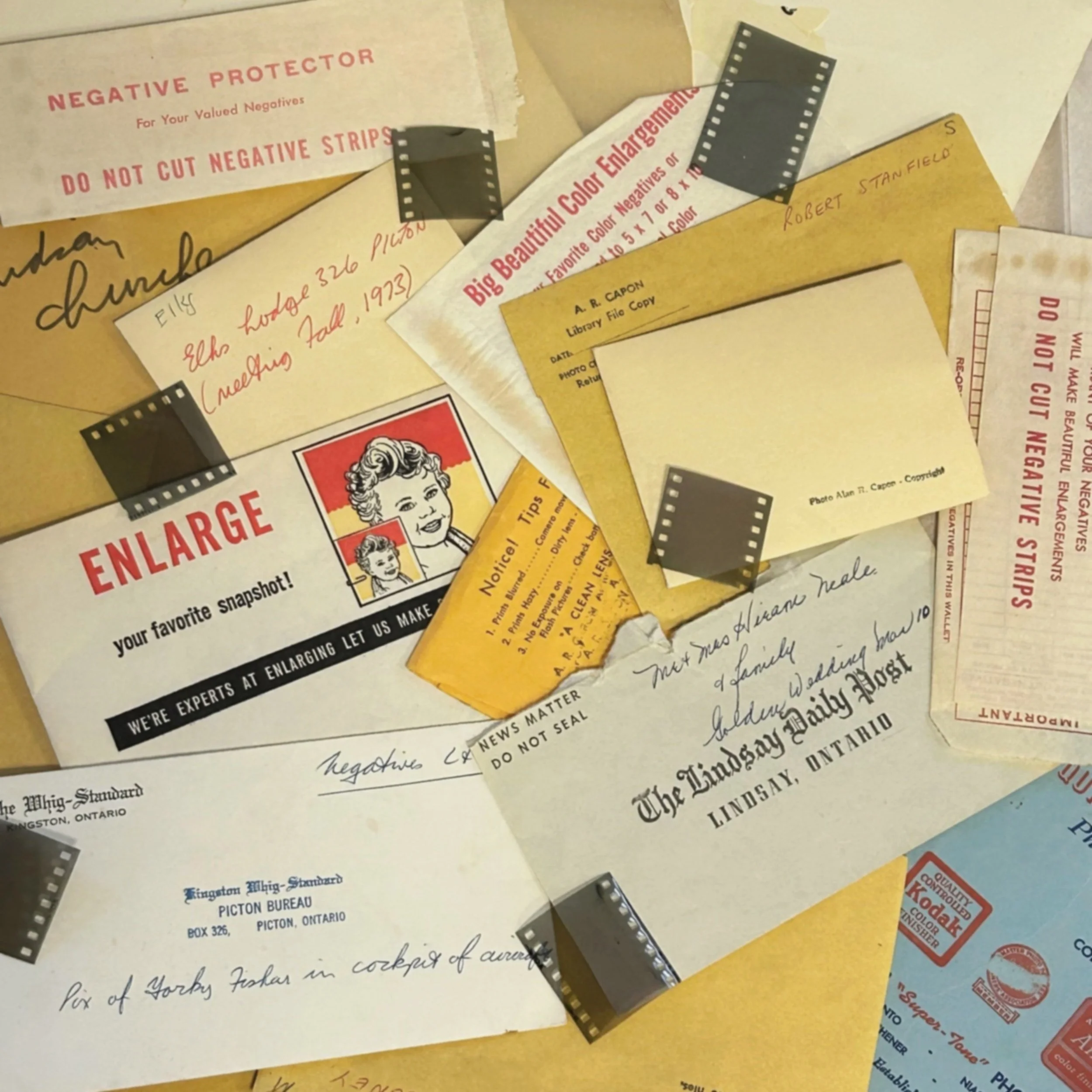 Collection of vintage photo envelopes, film strips, and handwritten notes, with references to photo enlargement services and photo negatives. Includes envelopes from Ontario newspapers.