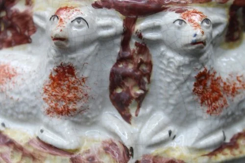 Close-up of two ceramic sheep with red markings on a decorative surface.