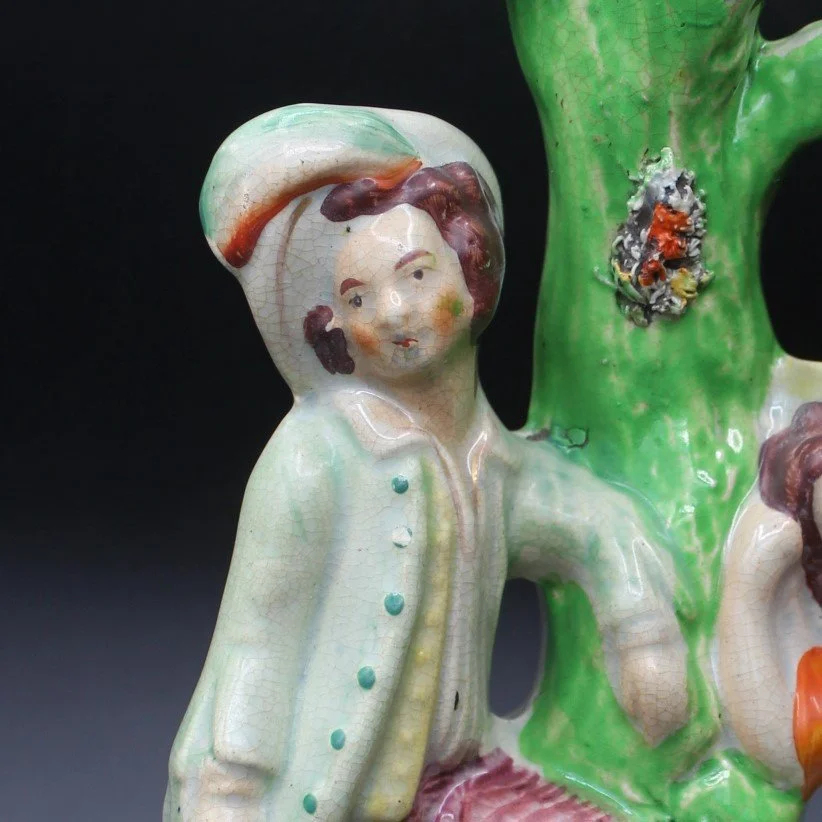 Ceramic figurine of a person in a green coat and hat, next to a green textured surface.