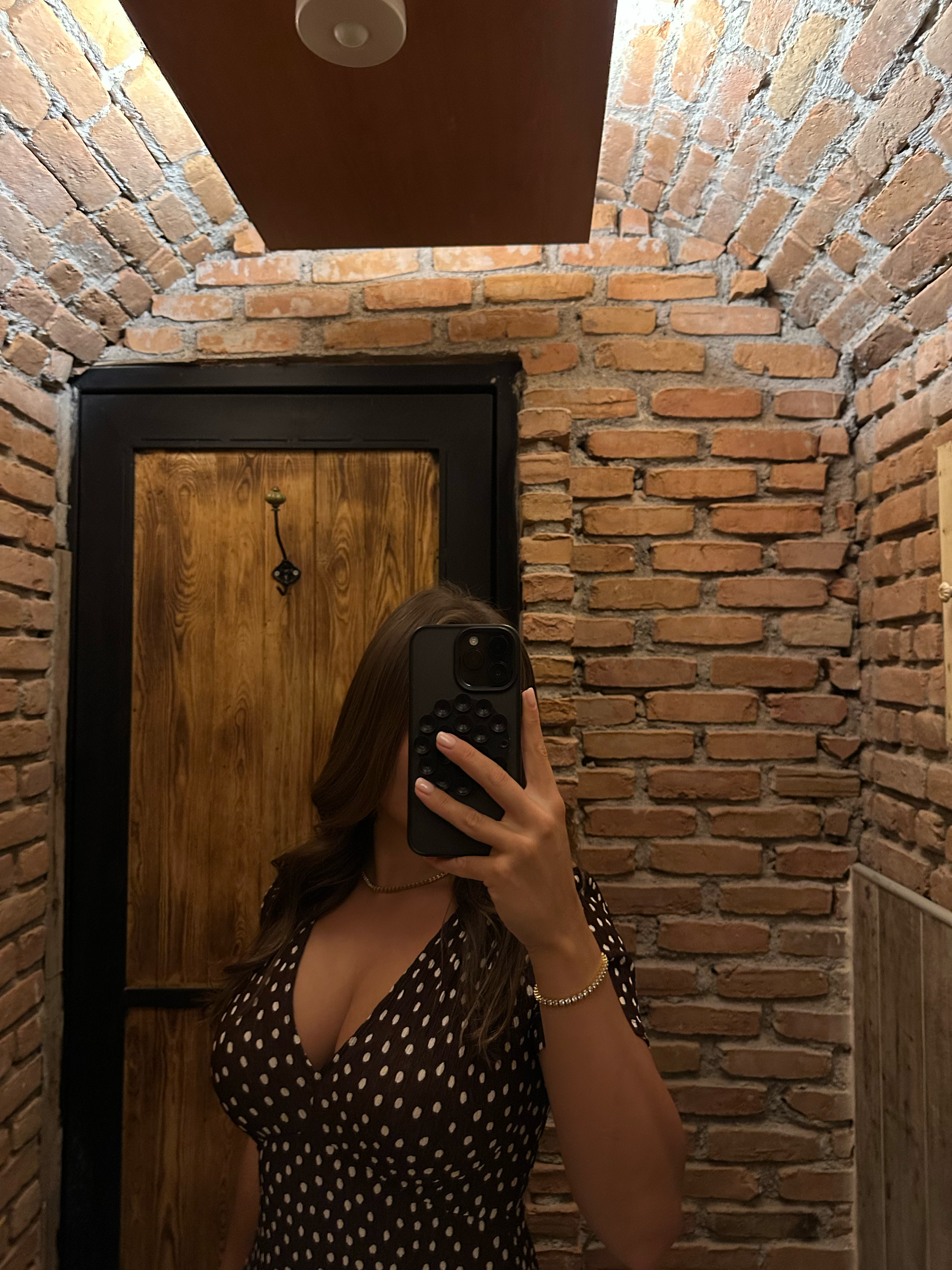 Arabella Blair, London’s top Independent Companion, taking a mirror selfie in a wine cellar, wearing a brown polka dot dress with a deep neckline.