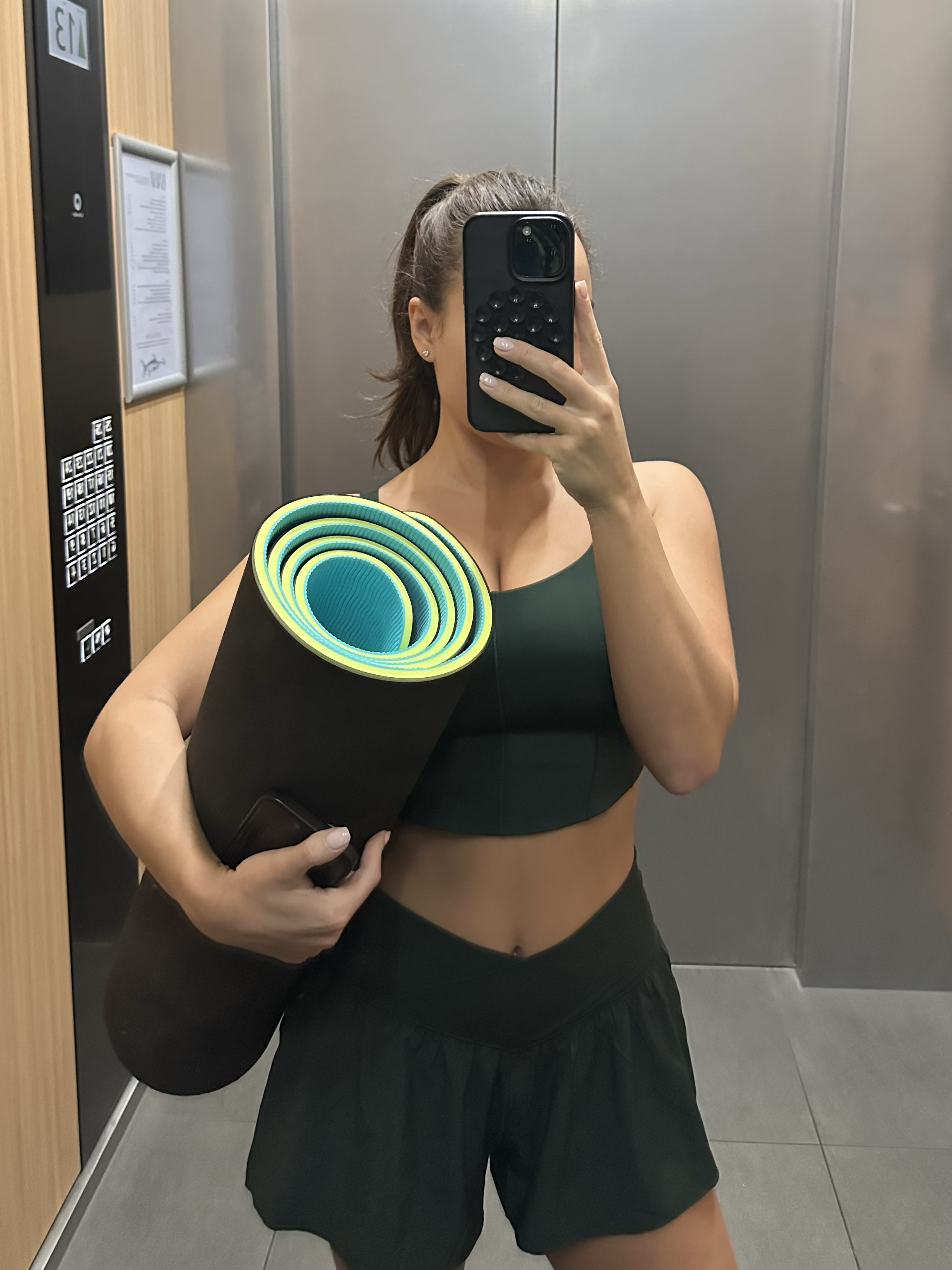 Arabella Blair, Luxury Independent Escort in London, in gym attire taking a mirror selfie in an elevator, holding a yoga mat under her arm.