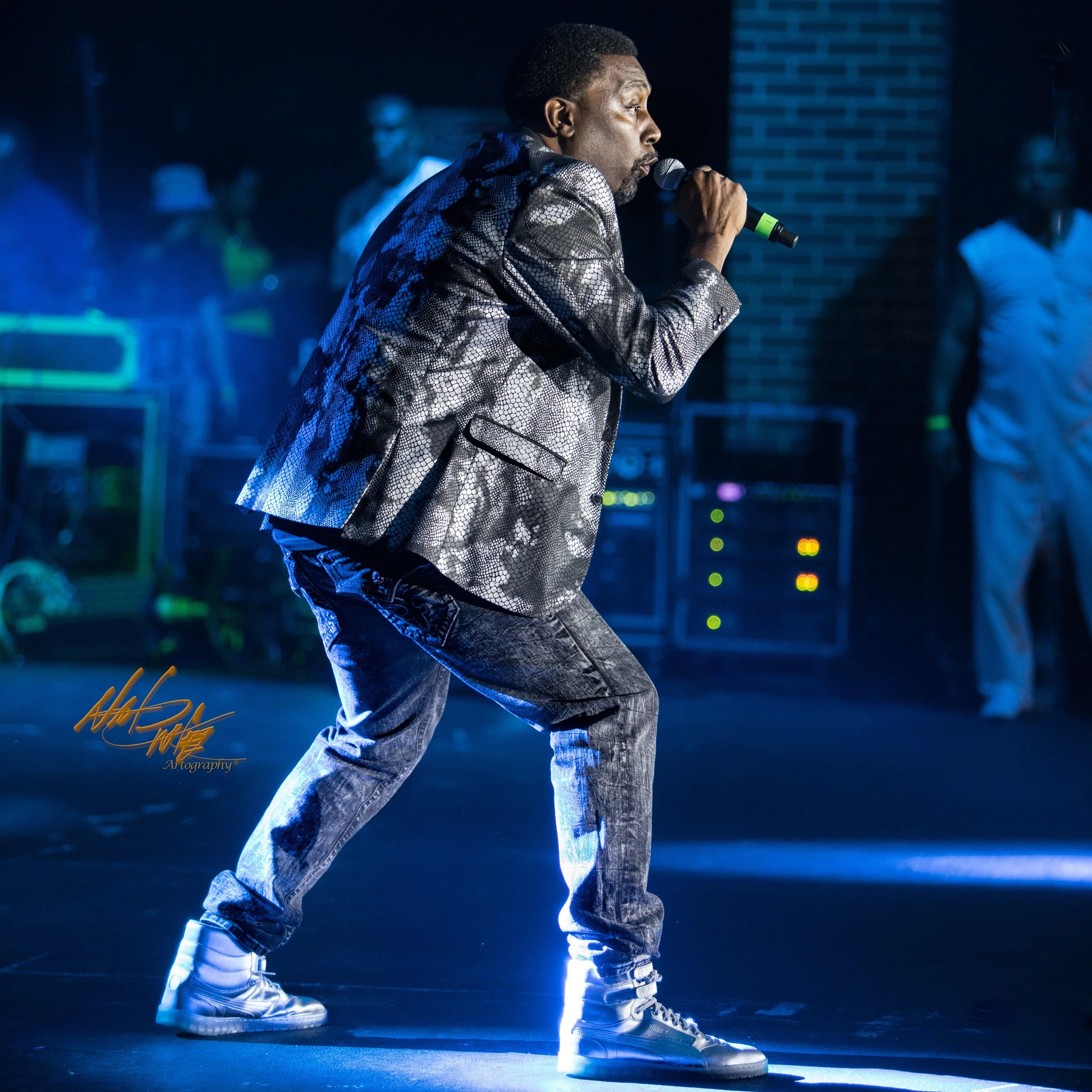 In this photo, Big Daddy Kane exudes confidence and power as he delivers his rhymes with skill and precision, his all-black outfit and signature gold chains shining under the bright lights. The vibrant colors of the stage and the sea of fans in the b