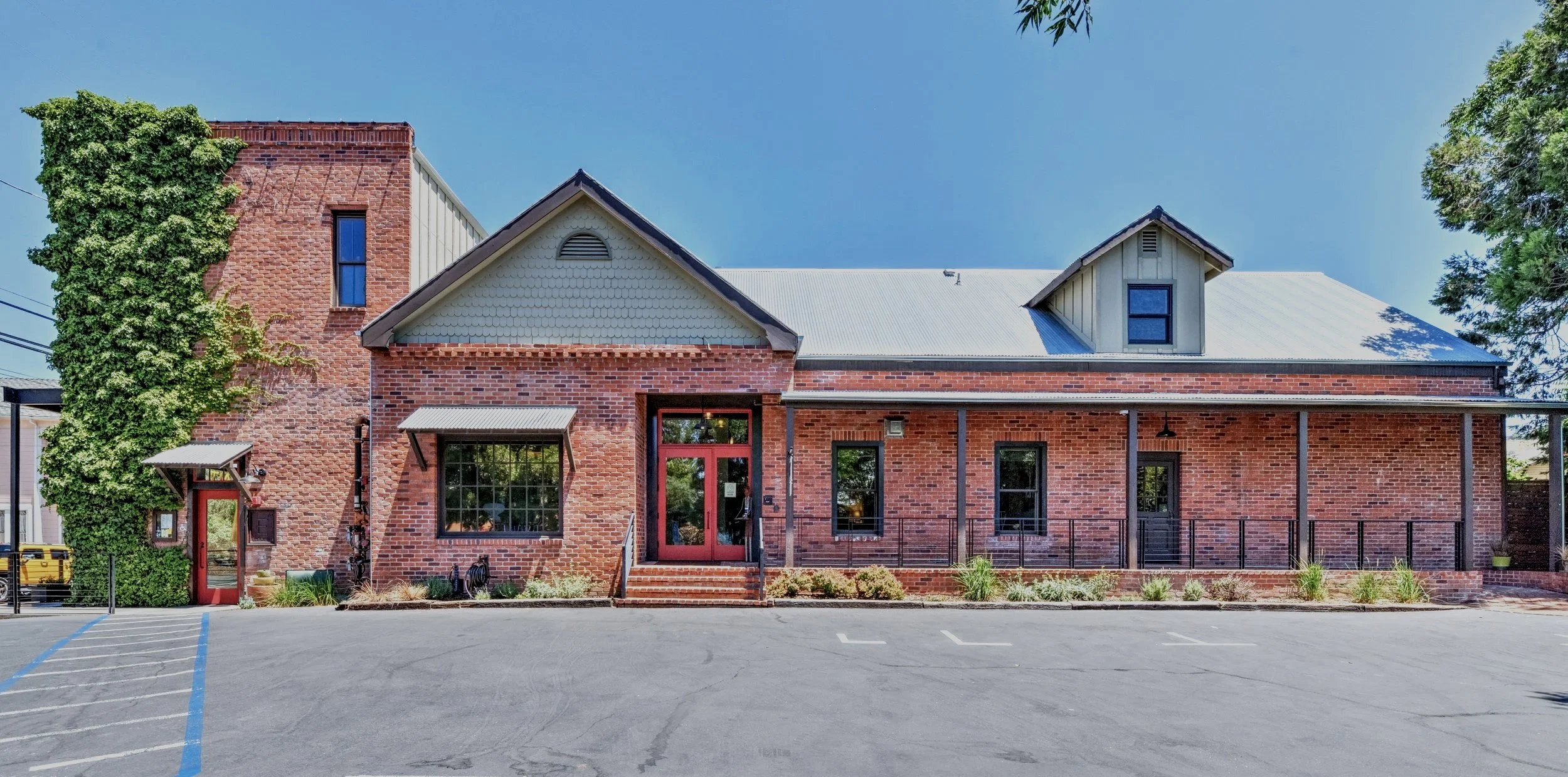 A brick building with a green garage door, gray roof, and signage on the door, surrounded by a parking lot with marked parking spaces, and trees in the background.
