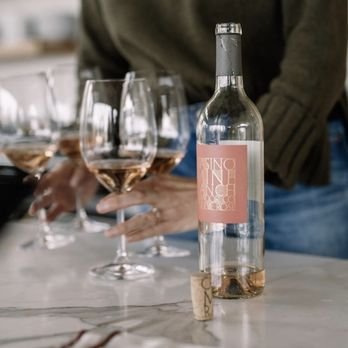A clear glass bottle with a pink label next to three glasses of rosé wine on a table.