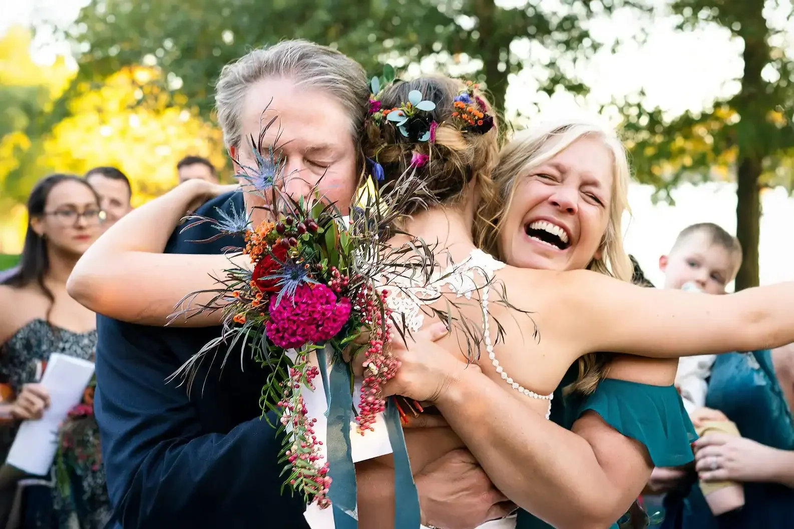An emotional moments of a bride hugging her parents after her wedding ceremony, holding a colorful bouquet at an outdoor wedding celebration in St. Louis, MO.