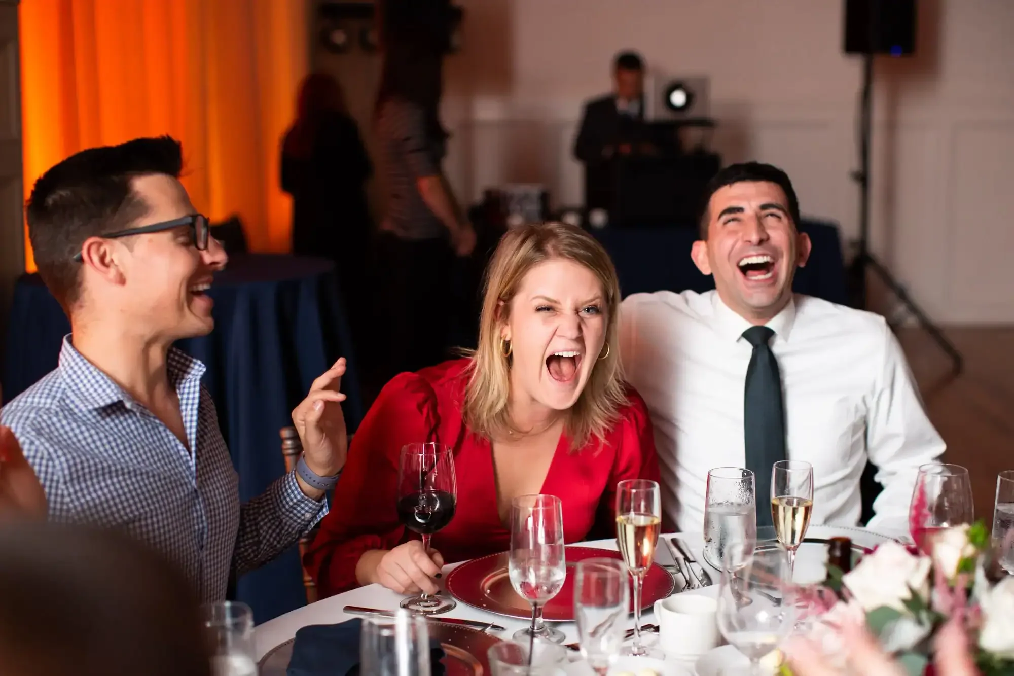 Guests laughing at their table at a St. Louis wedding reception with orange uplighting in the background.