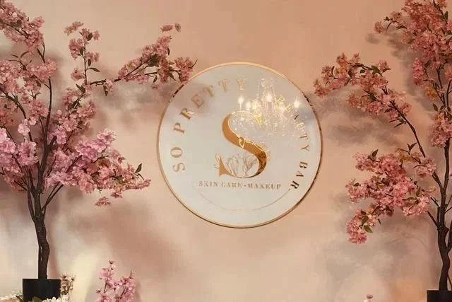 Interior wall with pink cherry blossom trees and a round sign that reads 'So Pretty by Beauty Bar, Skin Care + Makeup'
