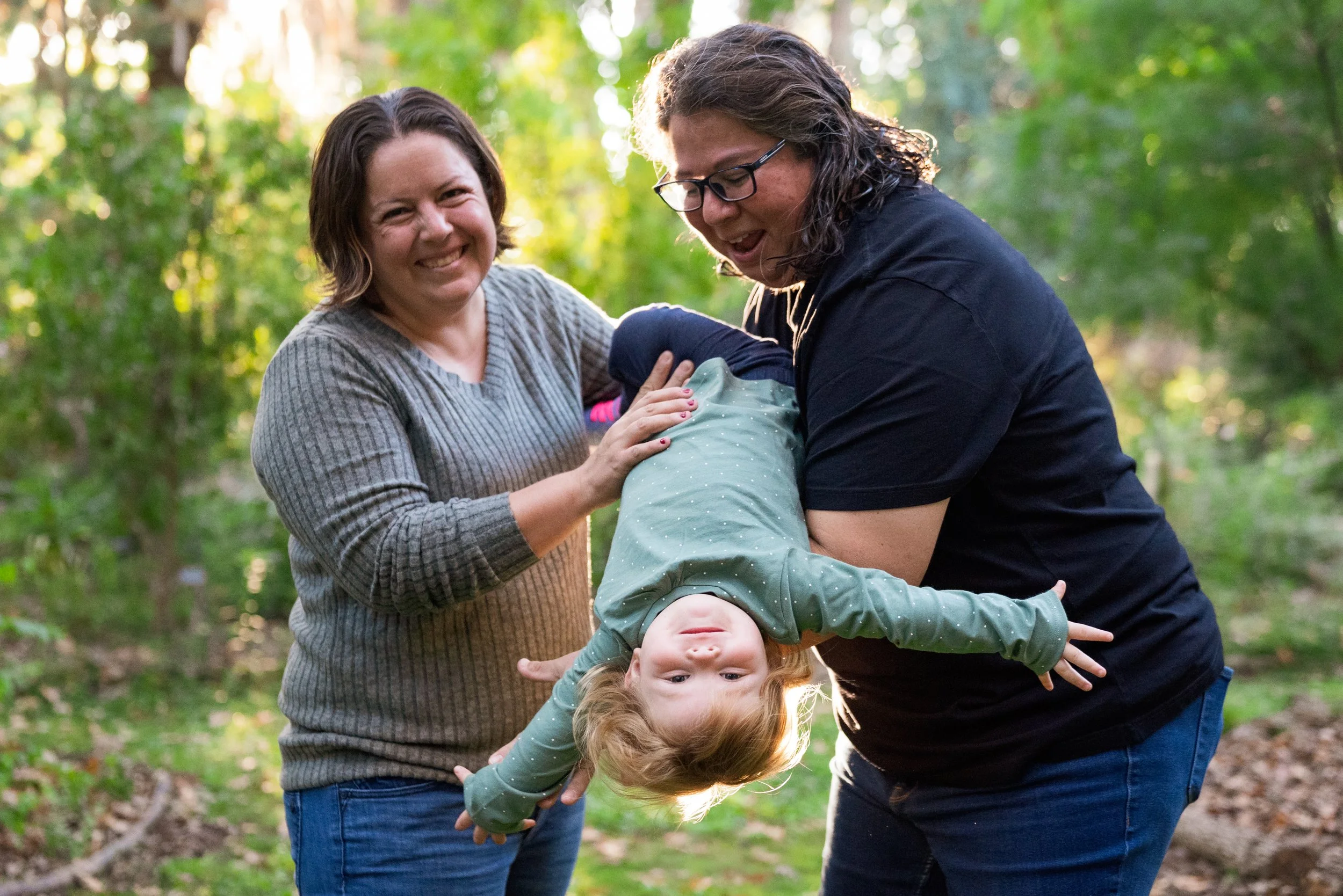 Lesbian couple holding their child upside down in a park playing with leaves