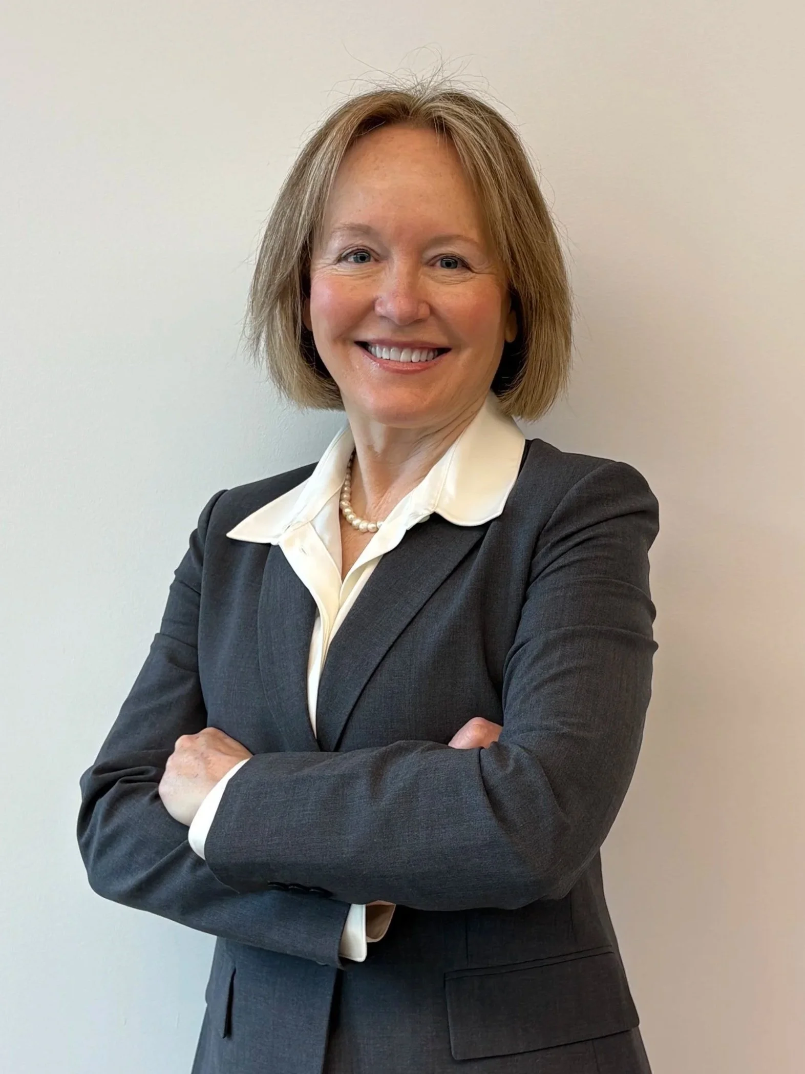 A professional woman with blonde, shoulder-length hair, smiling, wearing a black blazer and white shirt against a gray background.