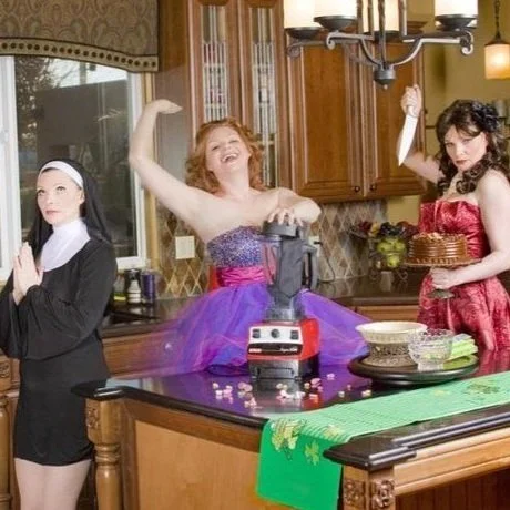 Blissom dressed as a nun, in a purple party dress, and holding a cake with a knife