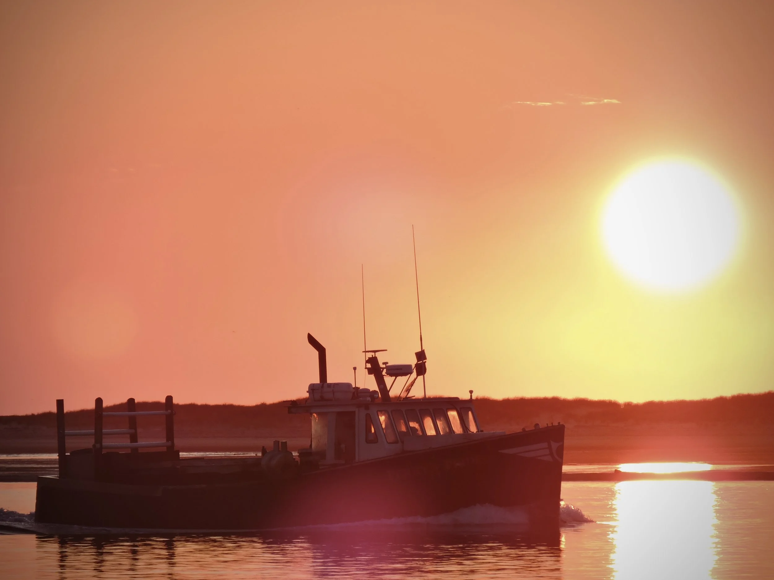 A boat on calm water during sunset or sunrise with orange and yellow sky. Equipment on the boat includes antennas and radar.