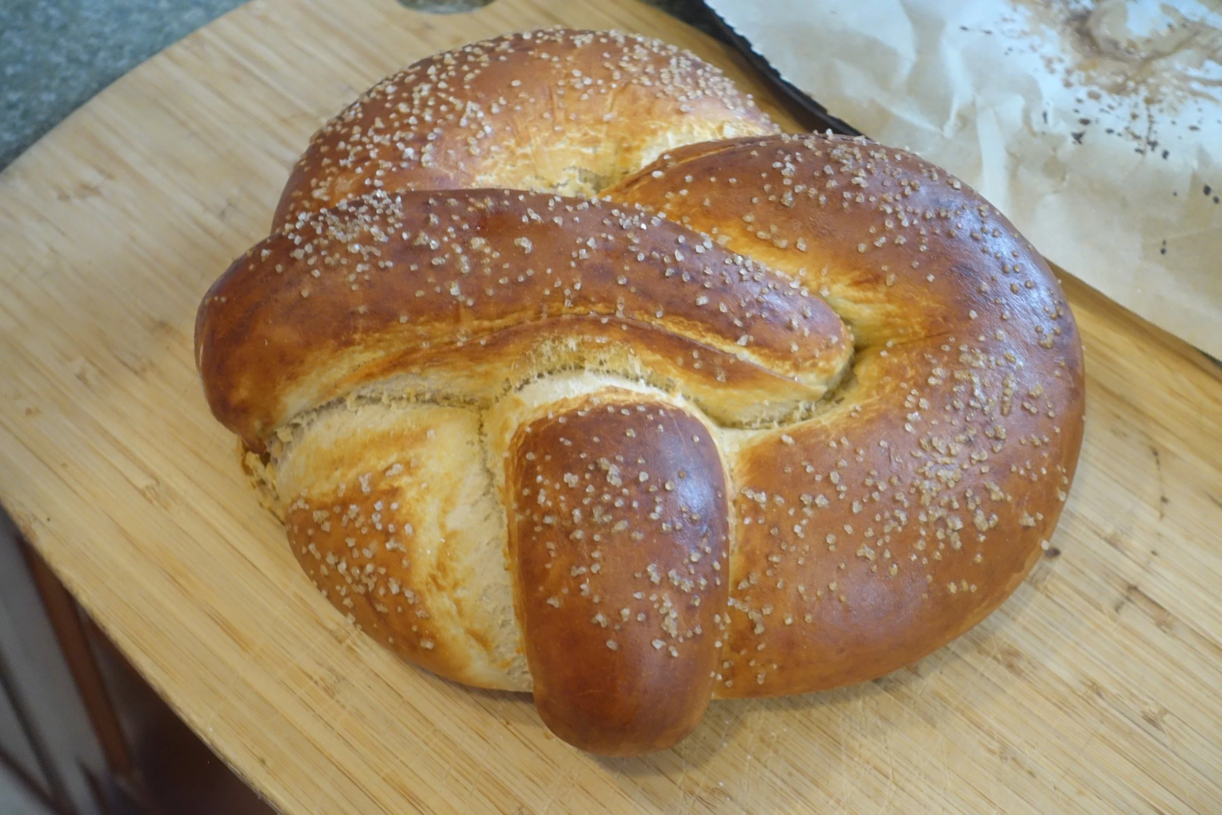 A freshly baked pretzel with coarse salt on top, placed on a wooden cutting board.