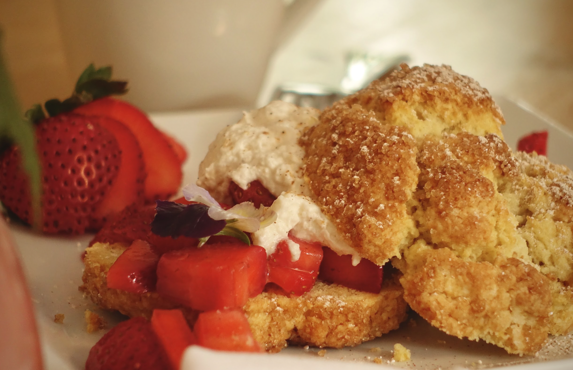 Close-up of a dessert plate featuring a slice of strawberry shortcake with fresh strawberries, whipped cream, and edible flower garnishes.
