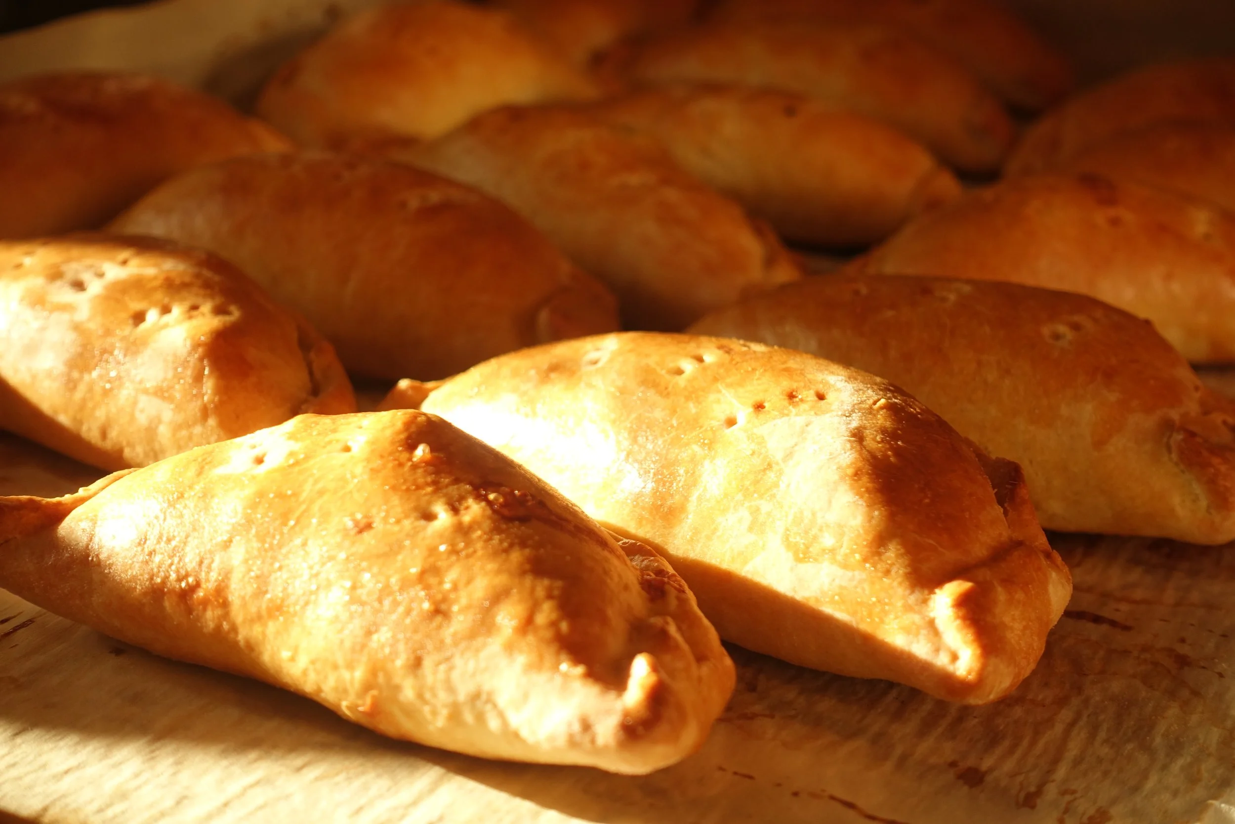 Close-up of freshly baked cooked empanadas with golden-brown crusts, resting on a wooden surface.