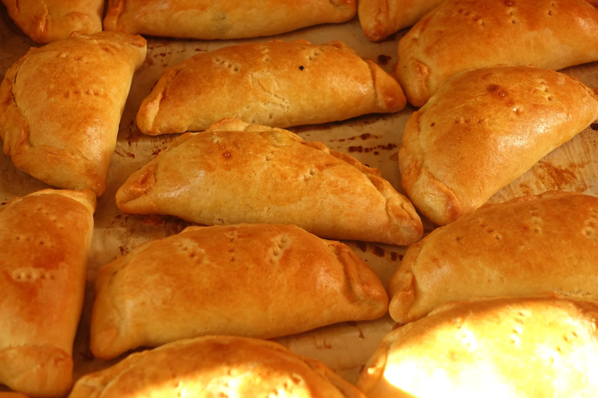 Baked golden-brown meat pies or calzones on a baking sheet.