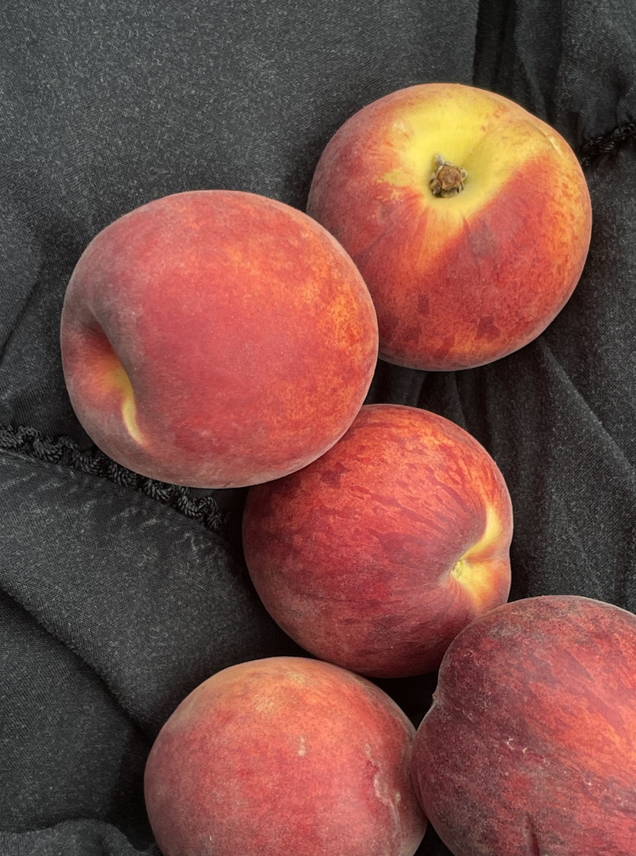 Six peaches on a dark fabric surface, showing their reddish-orange skin with some yellow hues.