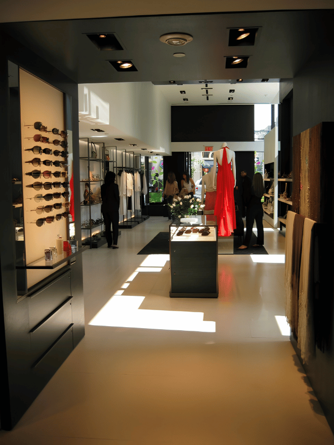 Interior of a boutique clothing store with mannequins, clothing racks, sunglasses display, and shoppers browsing.