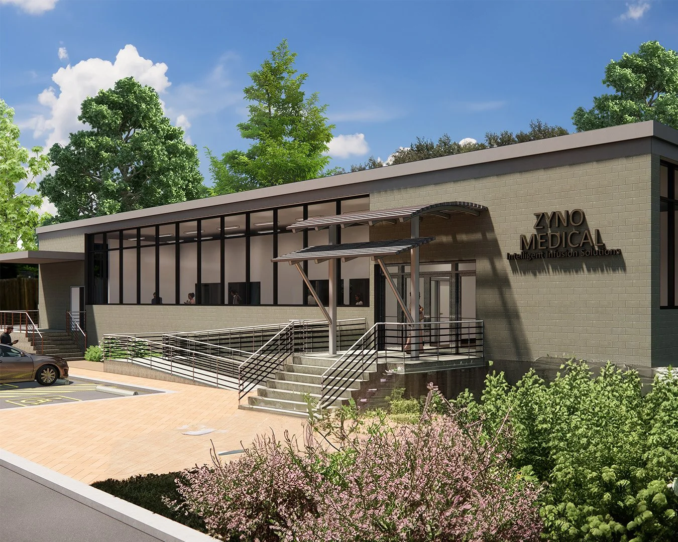 A modern medical building labeled ZYNO MEDICAL with large glass windows, an outdoor ramp with metal railings, stairs, and a landscaped area with pink flowers and green trees, under a blue sky.