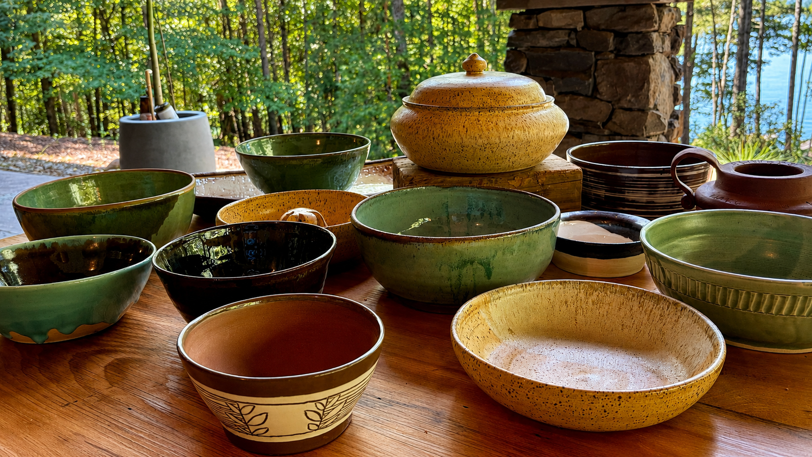 Colorful glazed ceramic bowls on a wooden table outdoors with a forest in the background.
