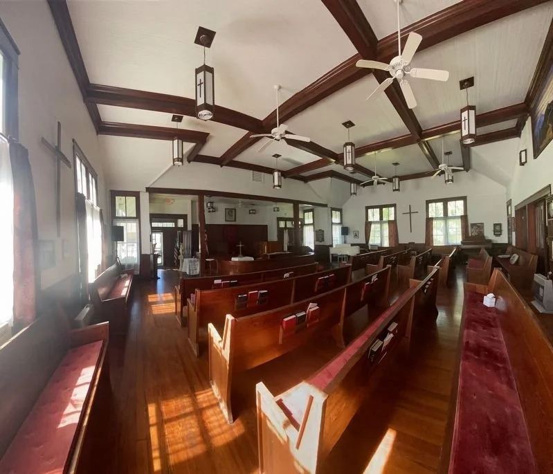 Interior of a church with wooden pews, a cross on the wall, and windows letting in natural light.
