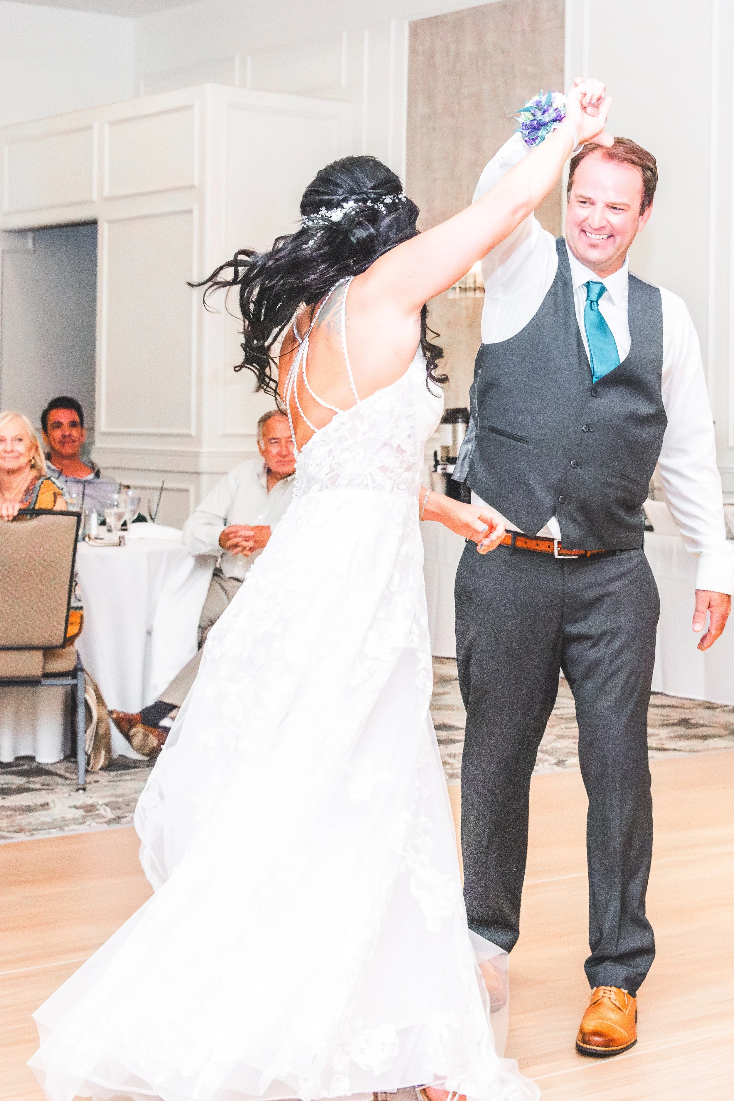 A bride and groom are dancing together at their wedding reception, with guests seated at tables watching in the background.
