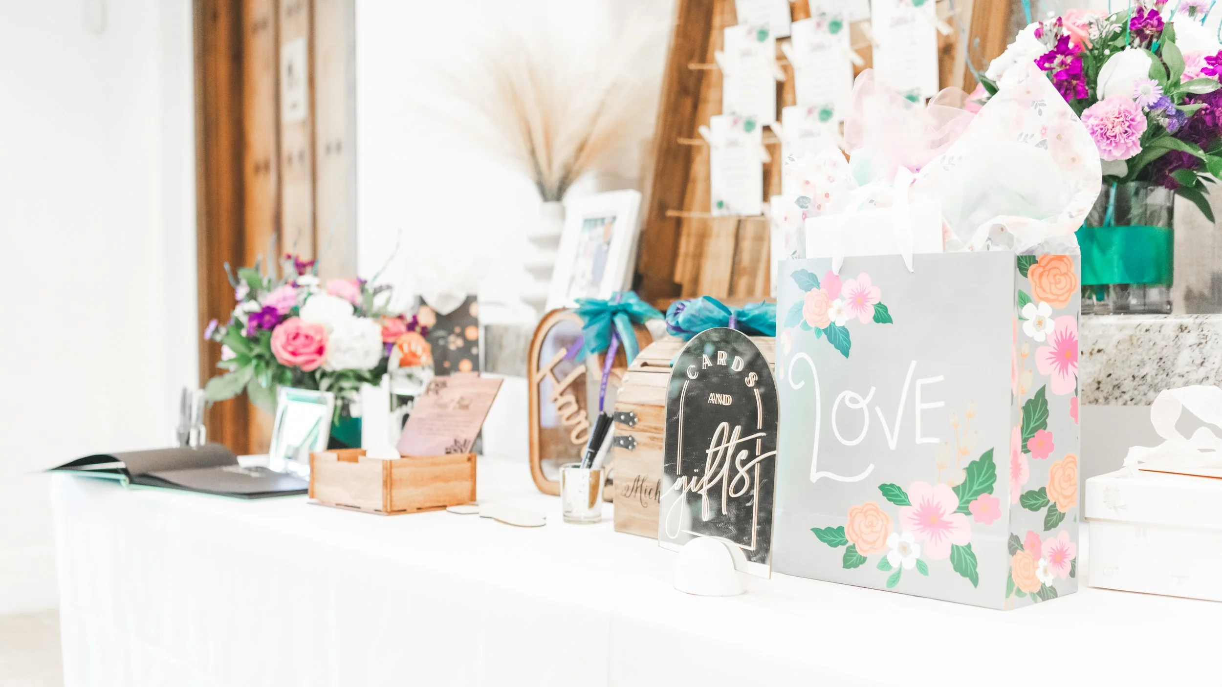 Decorative floral arrangements on a table at an event with signs reading "love" and "gifts" in the background.