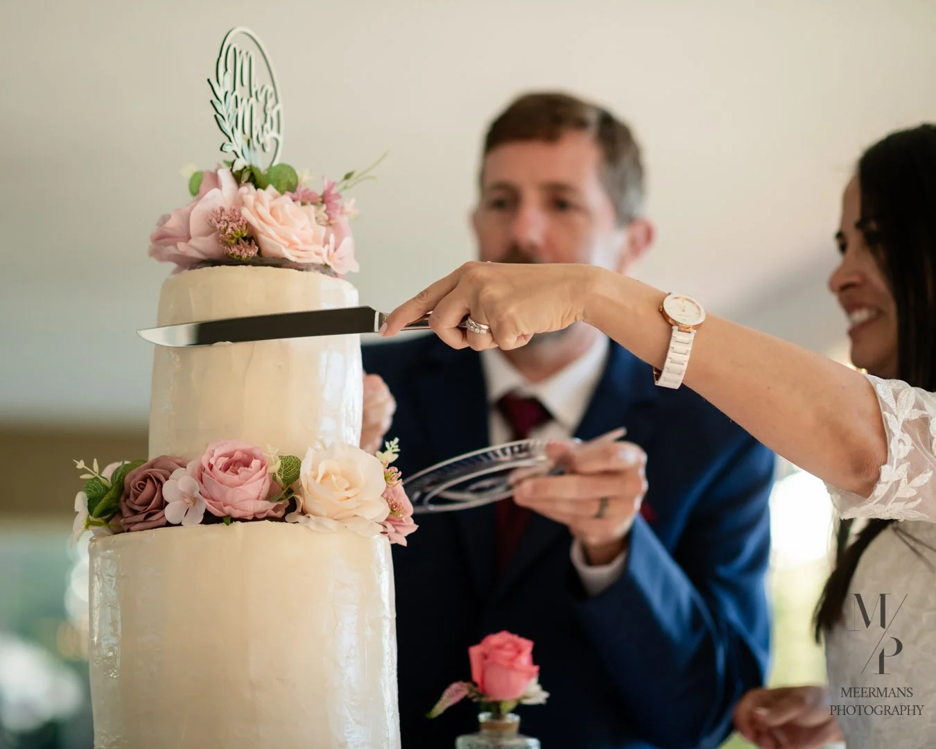 A bride and groom cutting a wedding cake decorated with pink and white flowers.