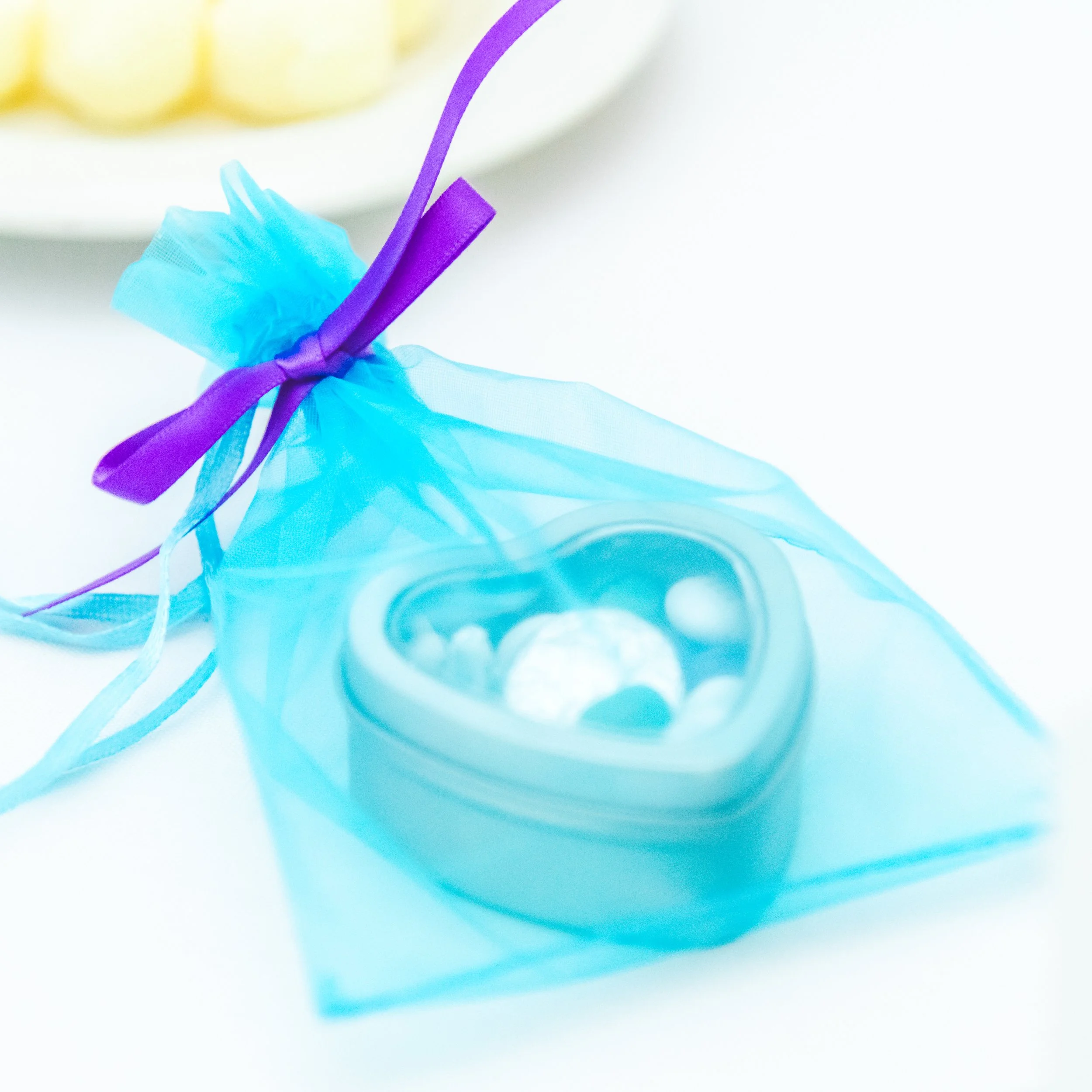 Close-up of a light blue sheer fabric with purple ribbon tying it, with gold-colored objects in the blurred background.
