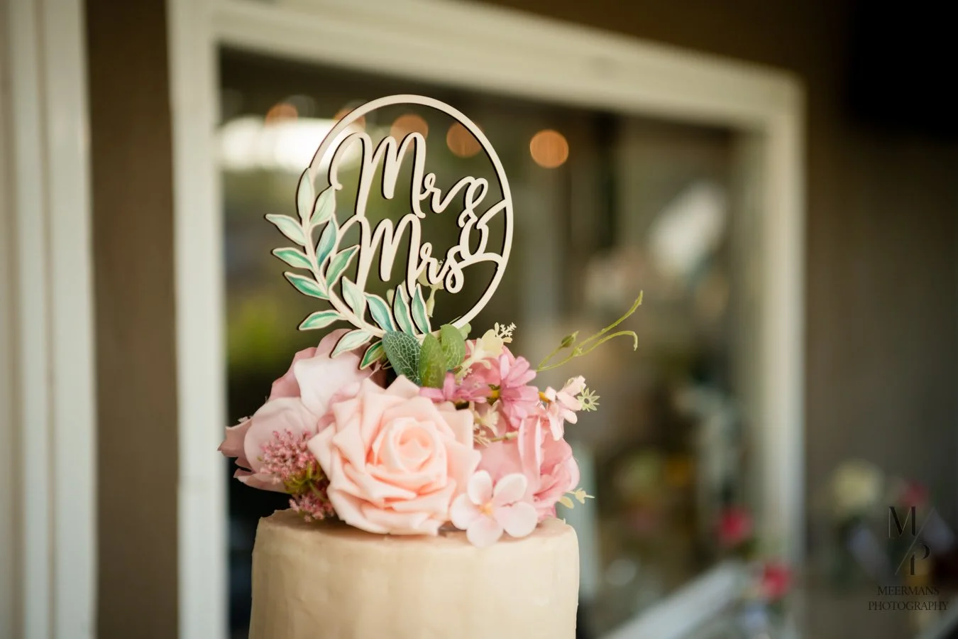 Wedding cake with pink roses, greenery, and a 'Mr & Mrs' cake topper