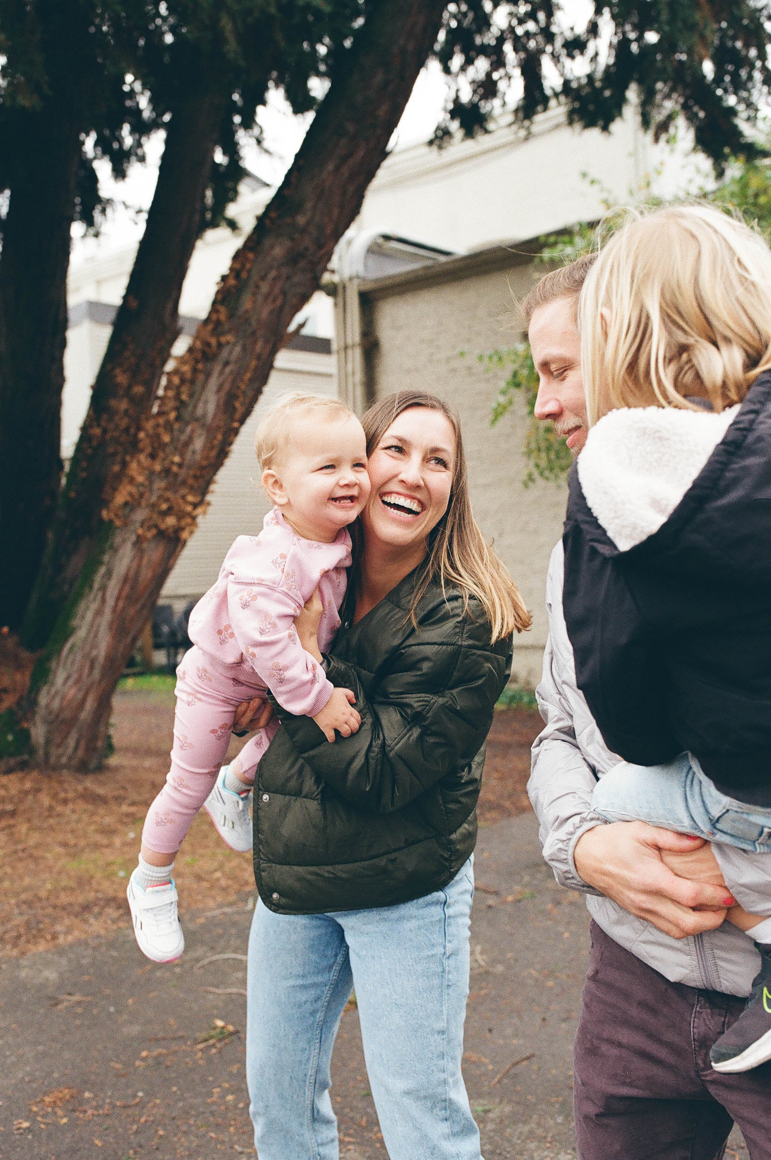 Happy family outdoors with two children, trees in background.