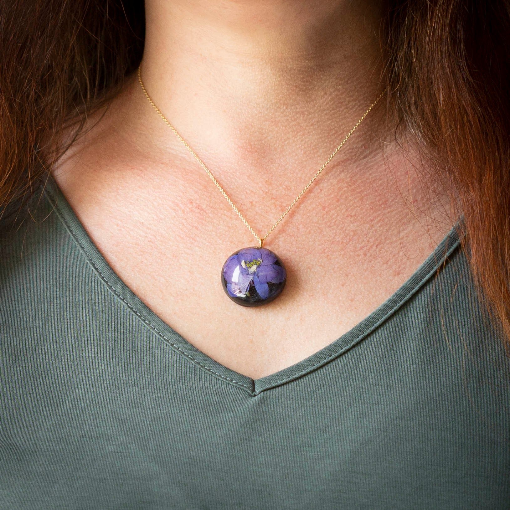 Beautiful real Purple Flower In a resin dome with a black clay back on a gold chain.
