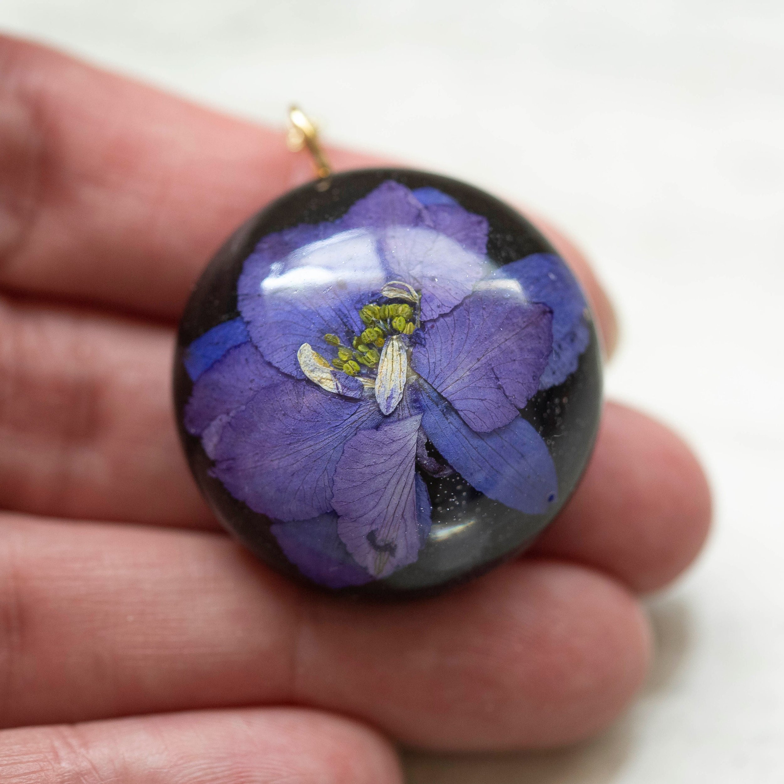 Beautiful real Purple Flower In a resin dome with a black clay back on a gold chain.