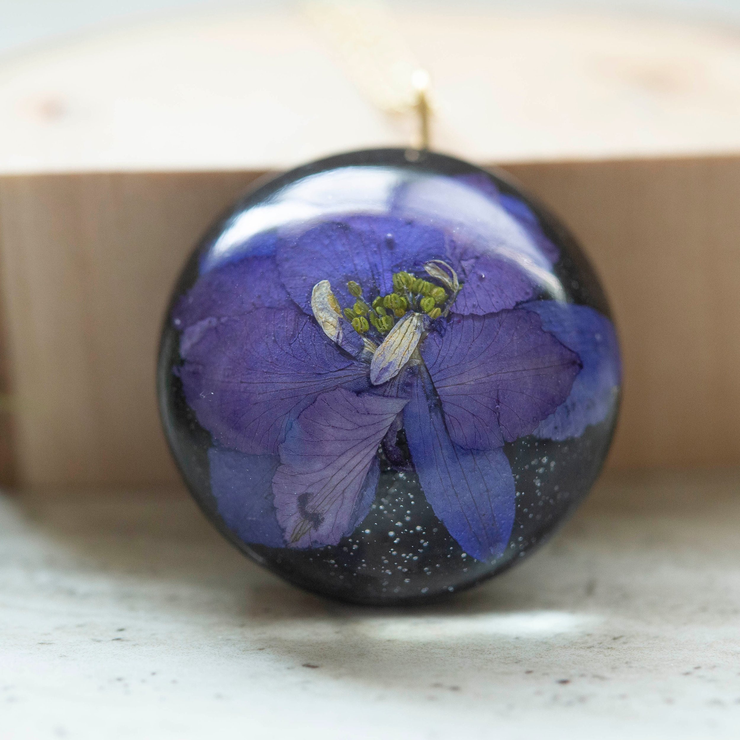 Beautiful real Purple Flower In a resin dome with a black clay back on a gold chain.
