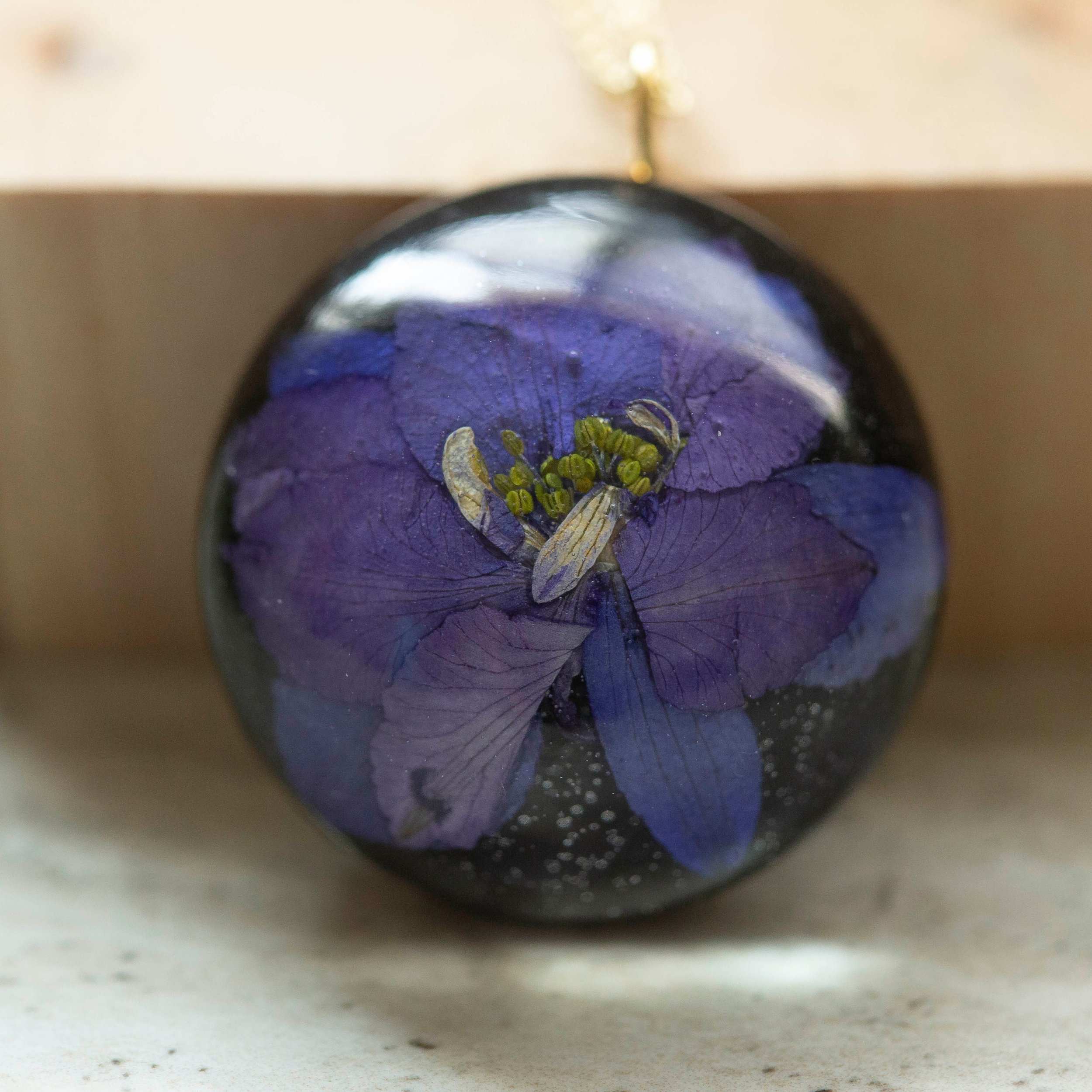 Beautiful real Purple Flower In a resin dome with a black clay back on a gold chain.