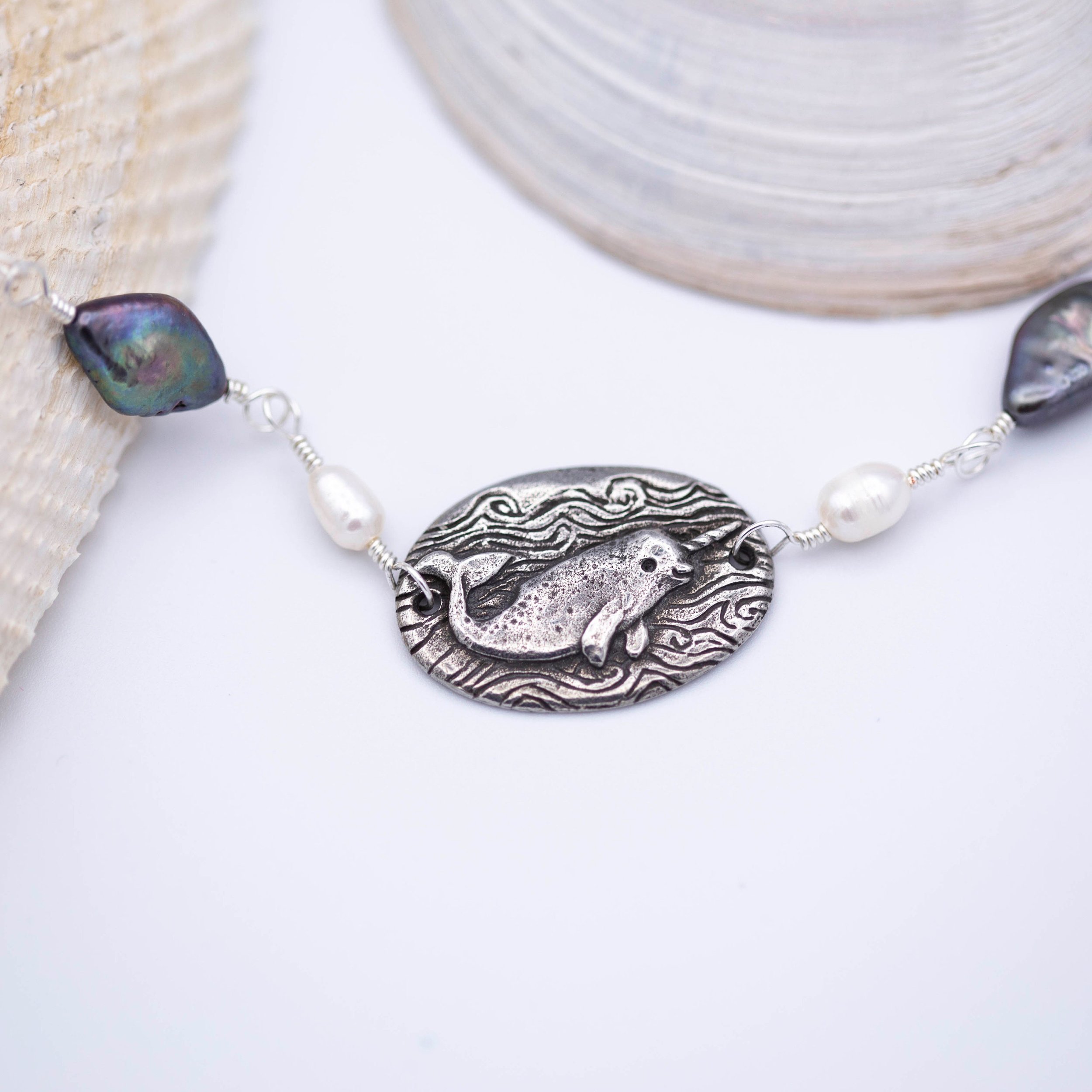 Sweet little narwhal pewter pendant with Magic is everywhere written on the back on a hand wrapped chain made of pearl and shell beads.